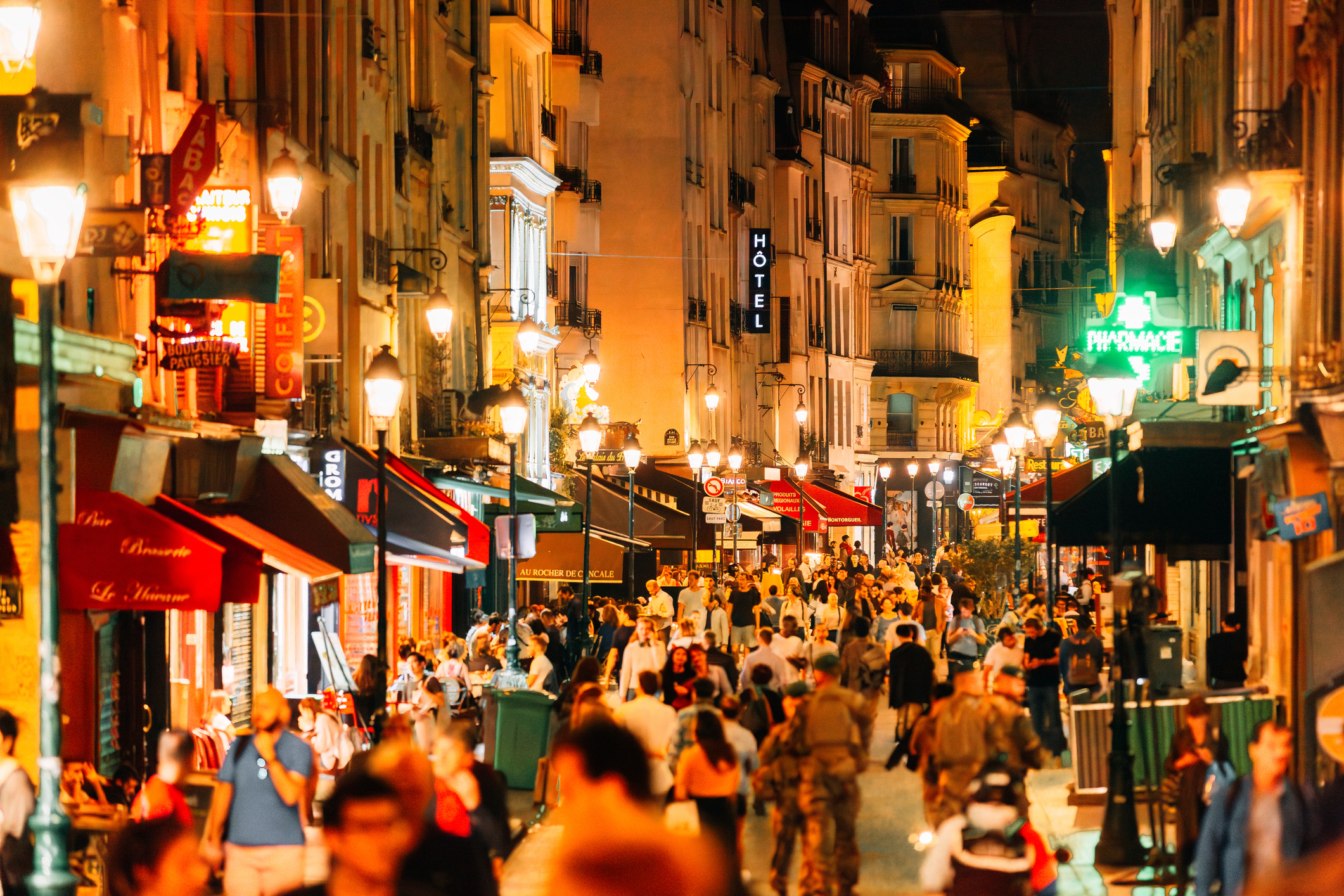 A bustling city street scene at night with illuminated shop signs and a crowd of pedestrians