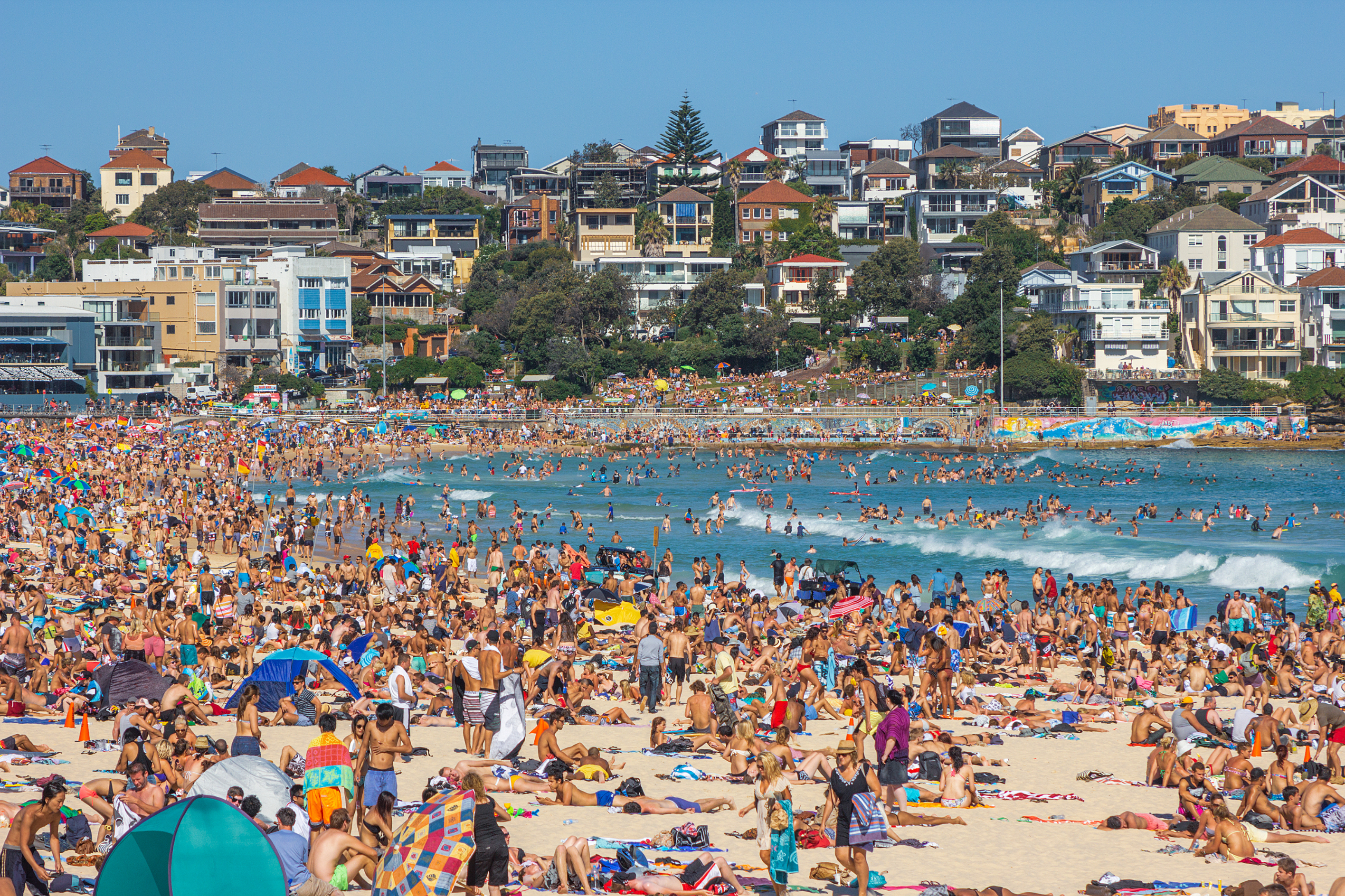 Crowded beach with people sunbathing and swimming, cityscape in the background