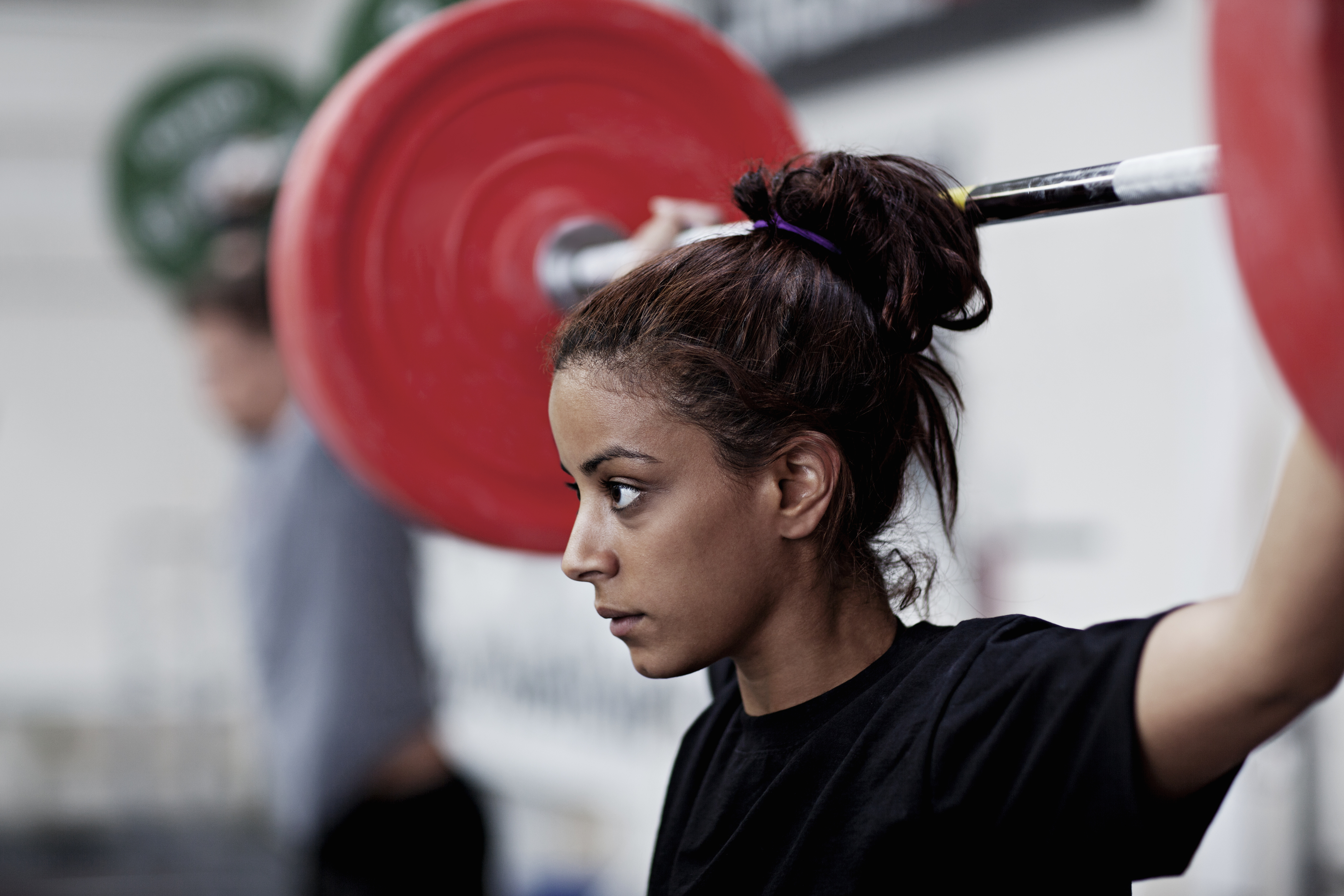 Woman lifting a barbell overhead in a gym setting, focused expression