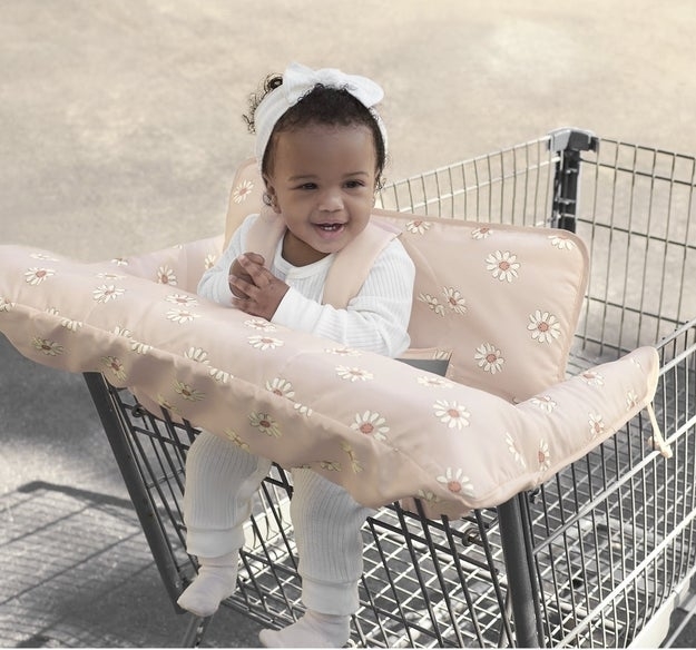 Smiling toddler sits in a shopping cart with a floral-patterned cushion insert for comfort
