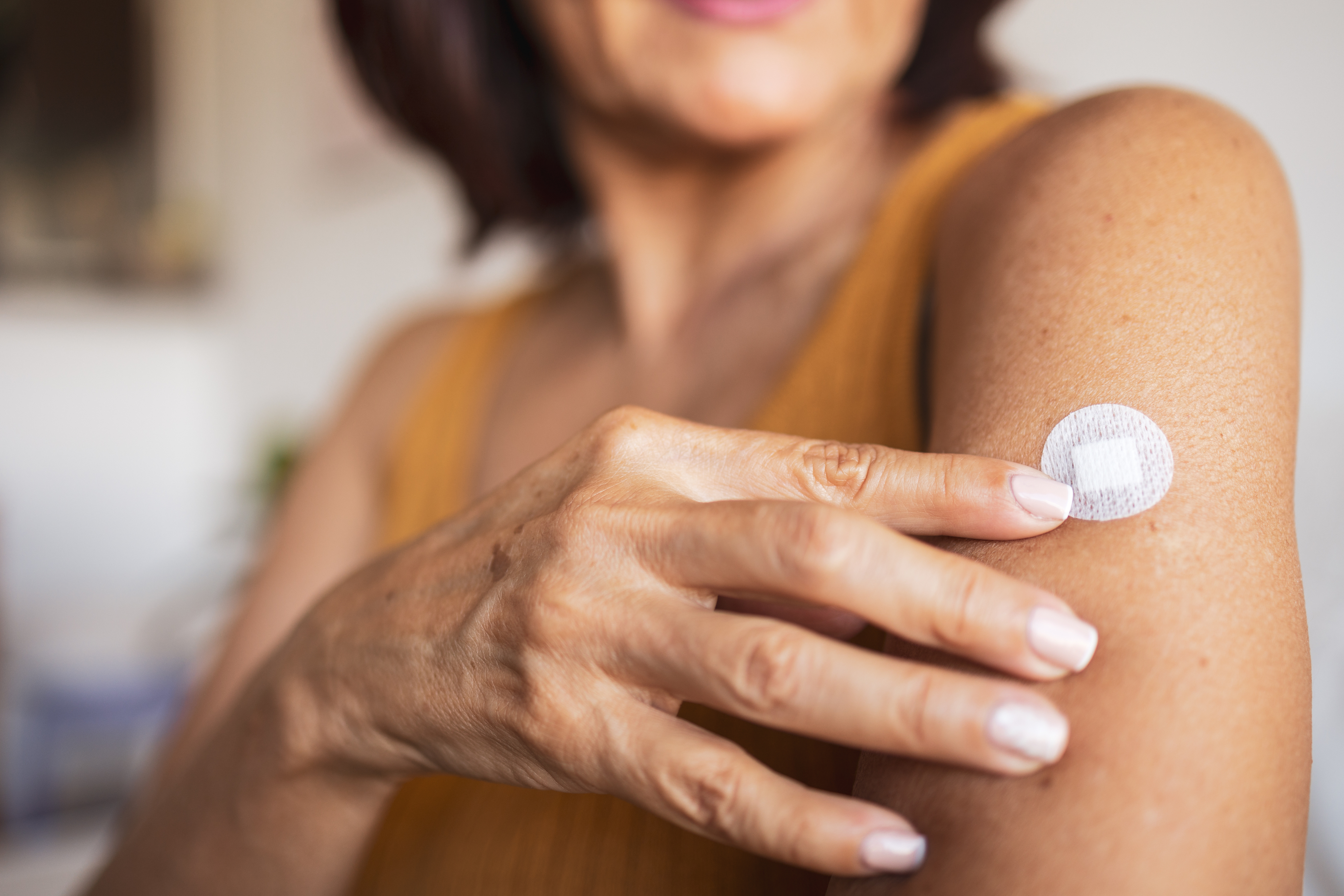 Woman attaching a hormone replacement patch to her upper arm