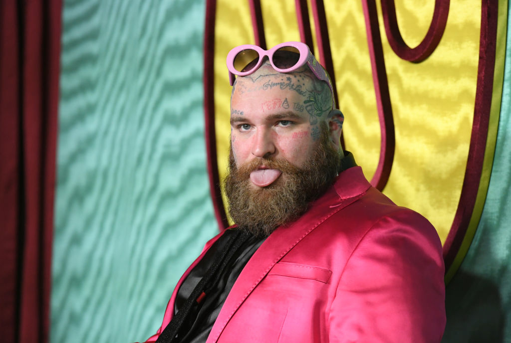 Teddy Swims in a pink suit with styled beard and pink sunglasses sticking out tongue at a themed event
