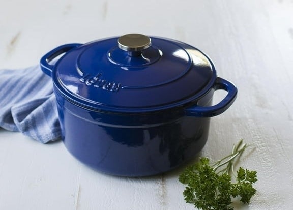 Blue enamel cast iron pot on a white wooden surface with a piece of green parsley nearby