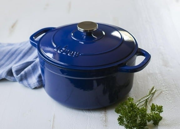 Blue enamel cast iron pot on a white wooden surface with a piece of green parsley nearby