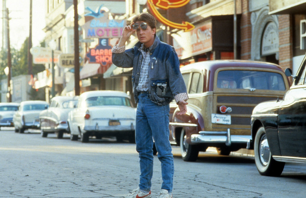 Marty McFly stands on a street in &quot;Back to the Future&quot;, wearing a denim jacket, vest, and holding sunglasses