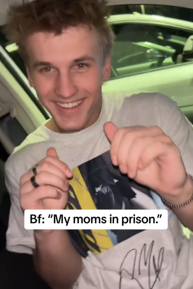 Smiling person in vehicle pointing at text on their shirt, with overlaid caption related to a family member being in prison