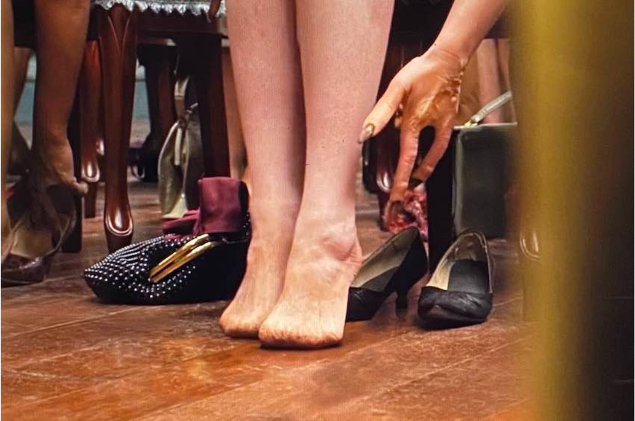 Barefoot person amid various shoes, reaching for one on the floor