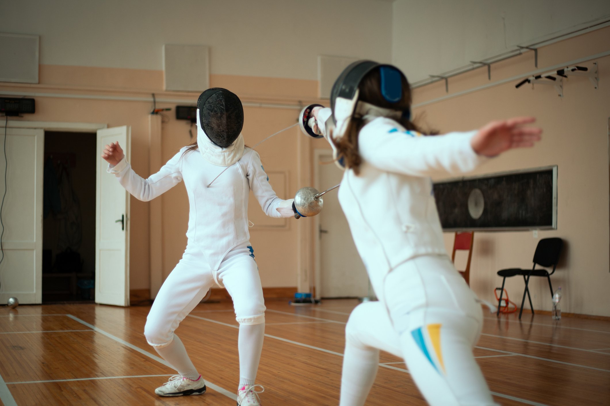 Two fencers in protective gear engaged in a match indoors
