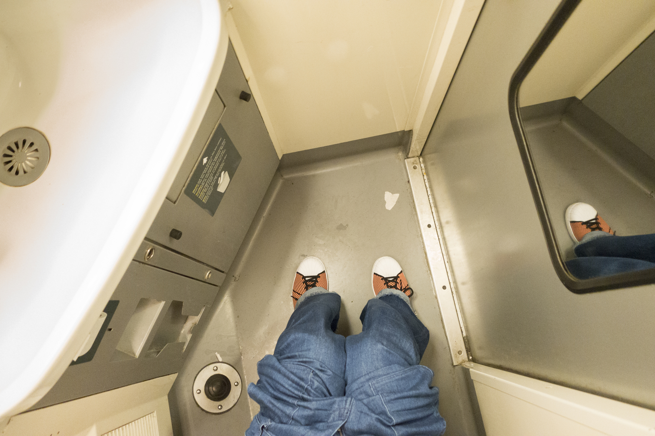 Person&#x27;s feet in sneakers standing inside an airplane lavatory