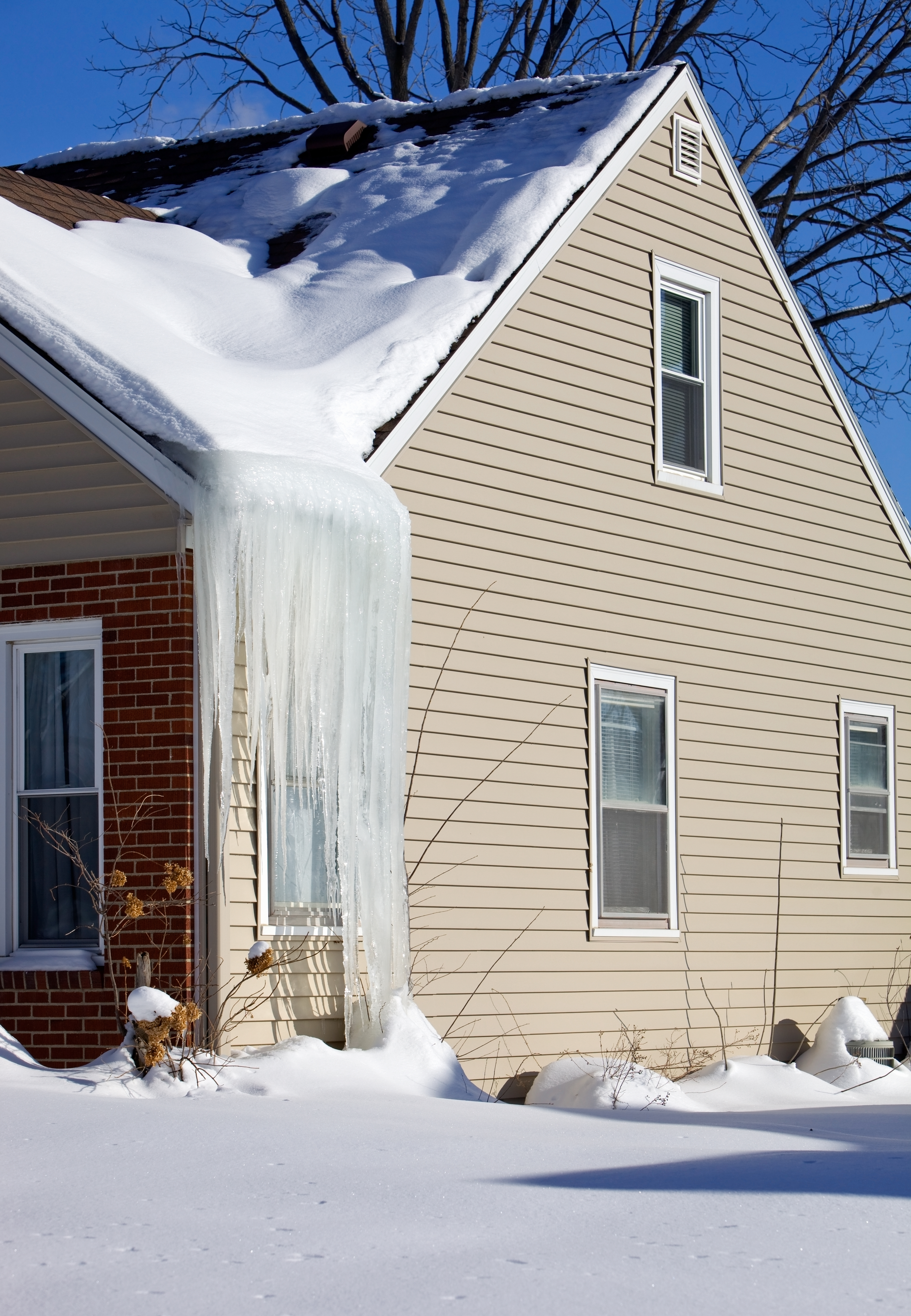 A house with large icicles hanging from the roof edge and snow-covered ground