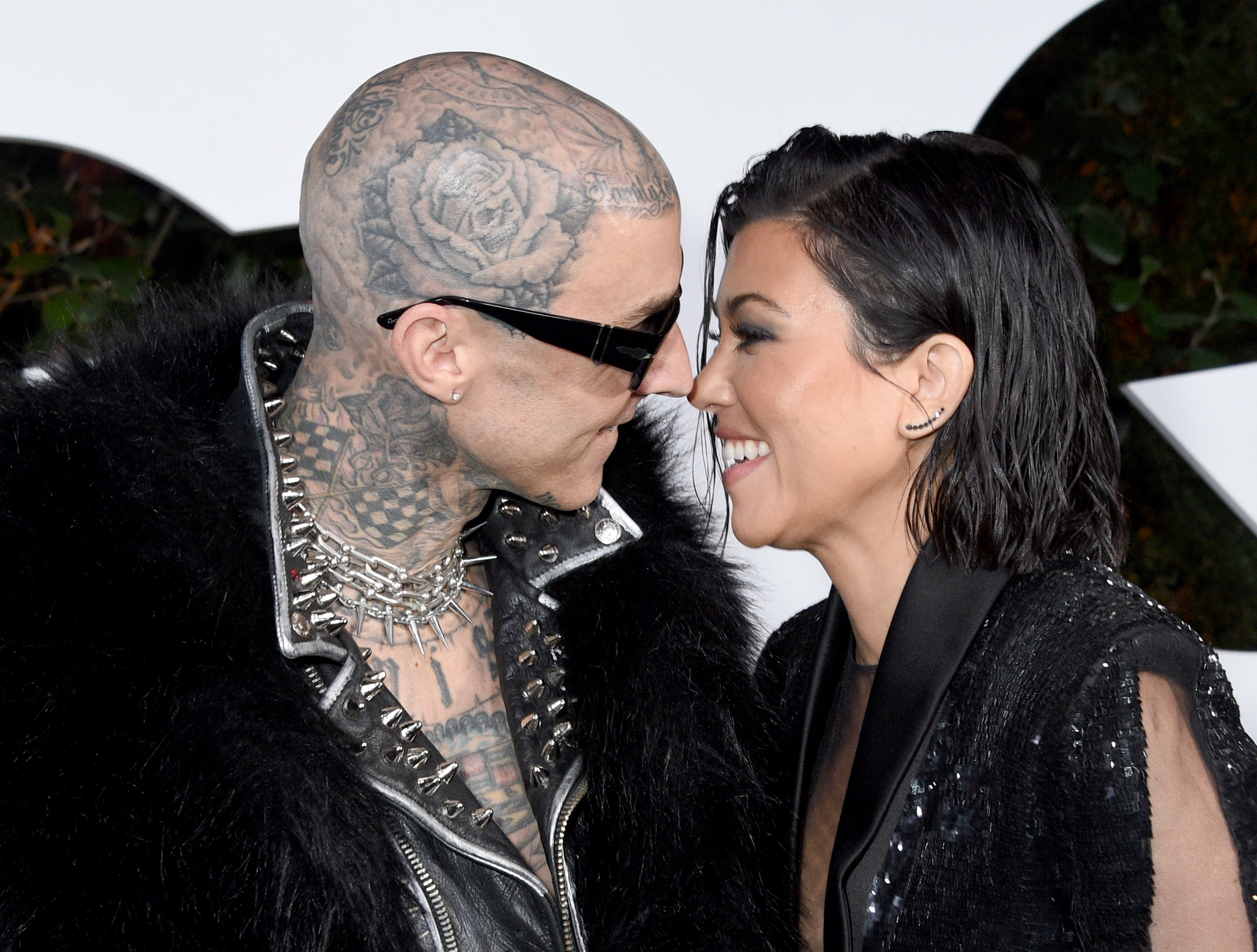 Two people smiling close to each other, one with tattoos and sunglasses, the other in a glittery dress