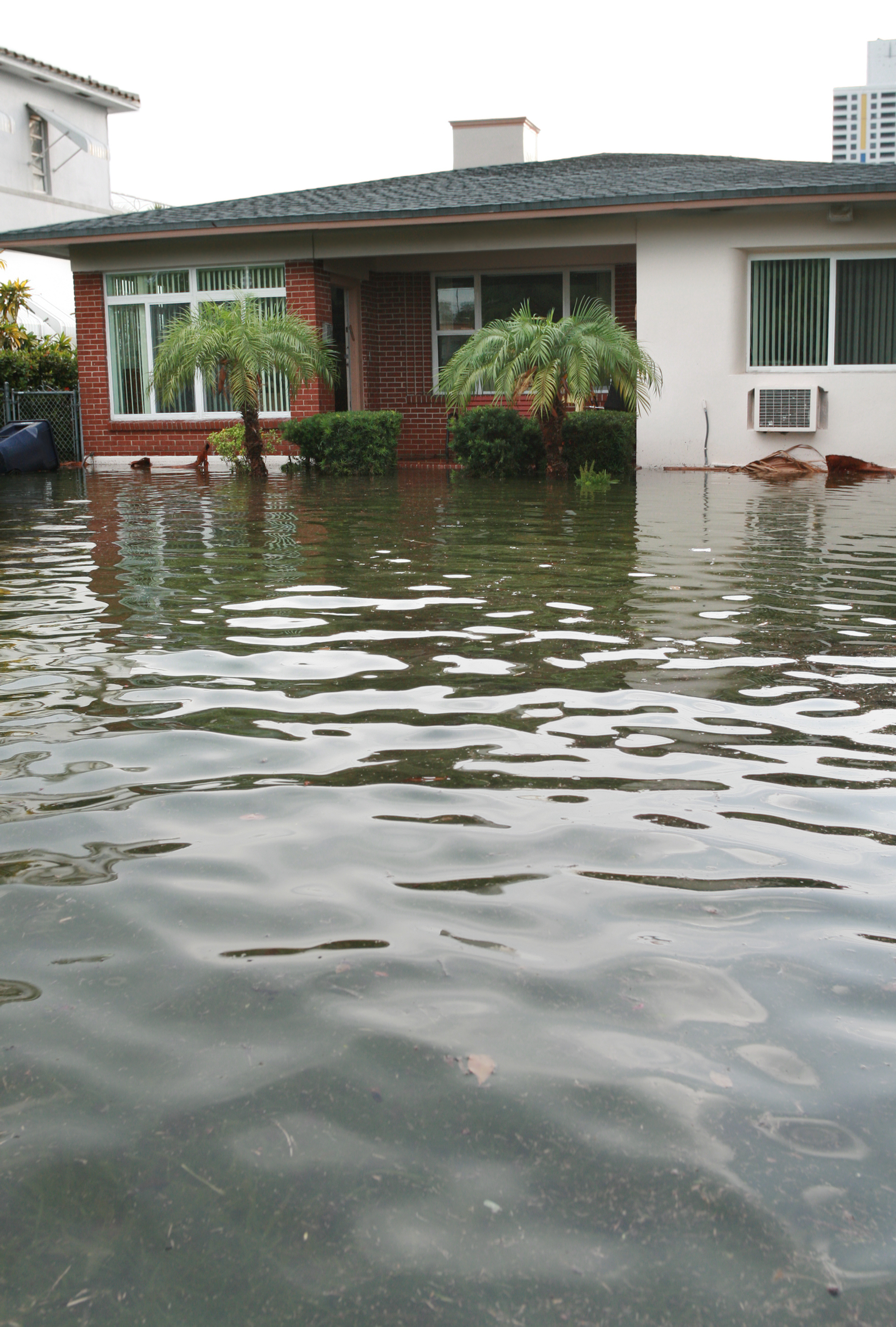 A flooded residential area with water reaching halfway up the front yard of a house