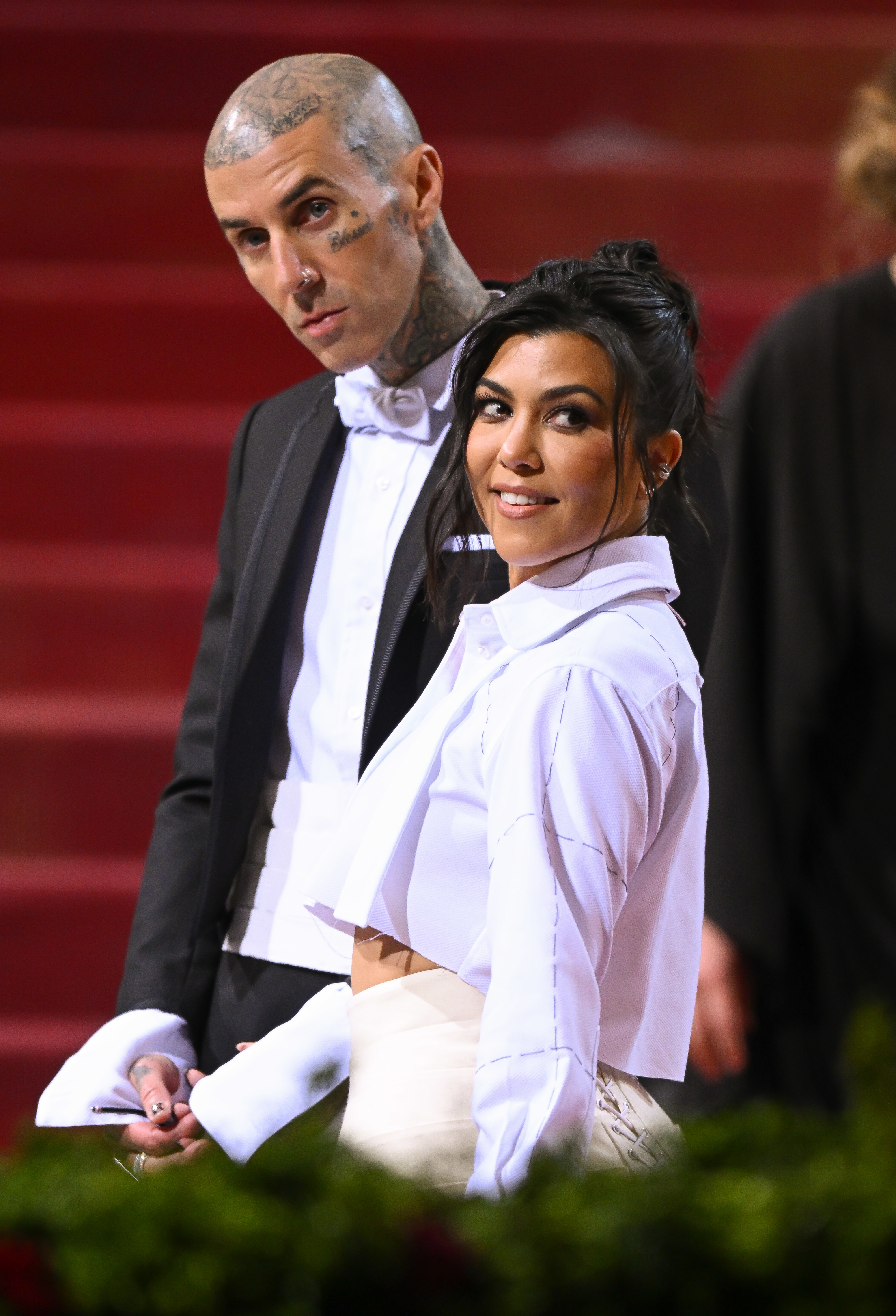 Two people at an event, one in a black tuxedo, the other in a white shirt and gloves