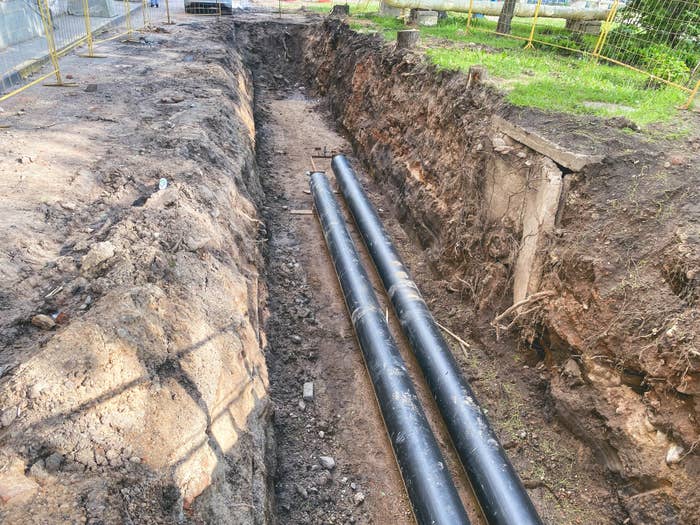 Trench with new black pipes laid for underground utilities, surrounded by dirt and enclosed by a yellow safety fence