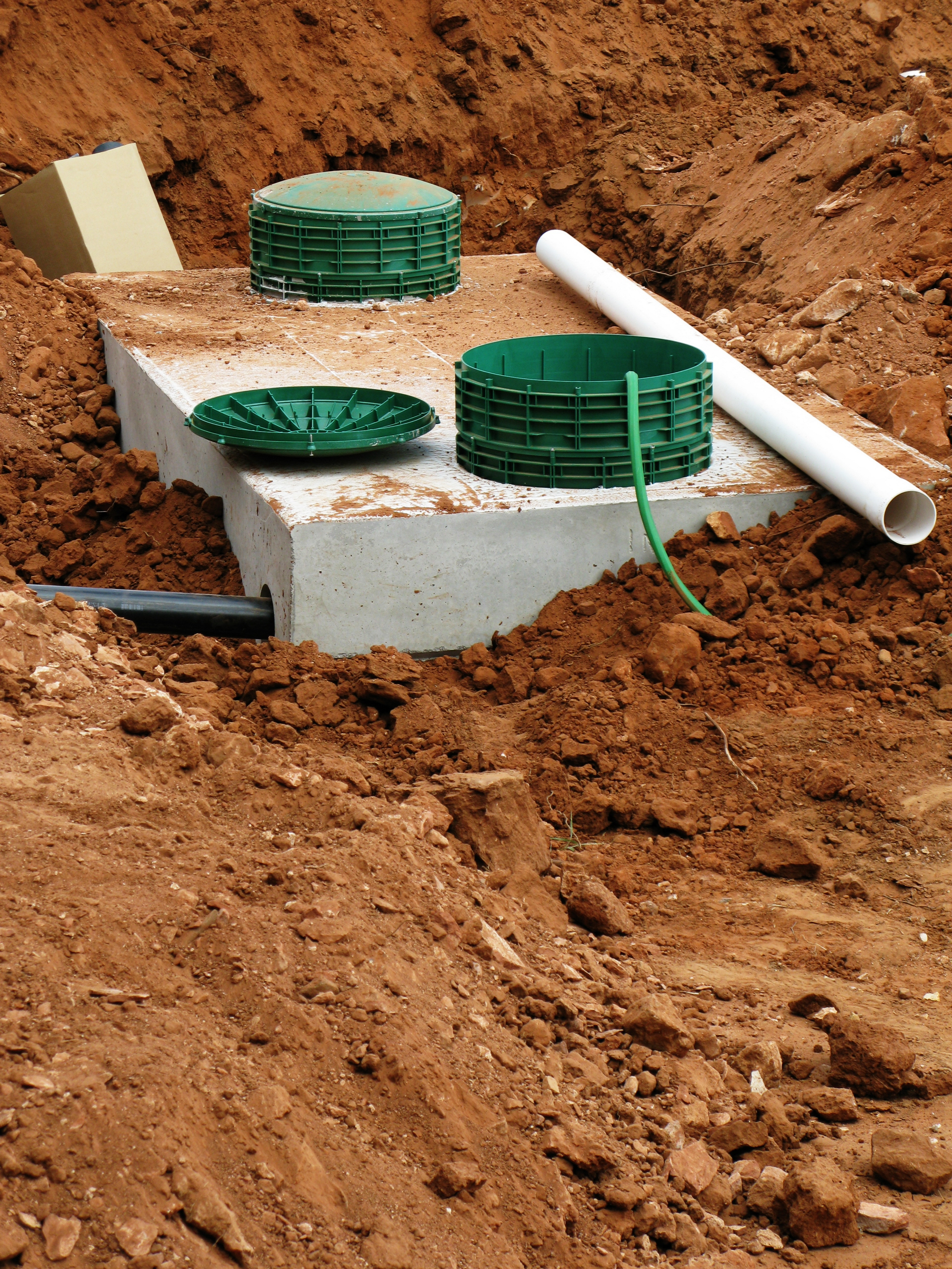 Septic tank installation in progress with exposed pipes and green lids on a construction site
