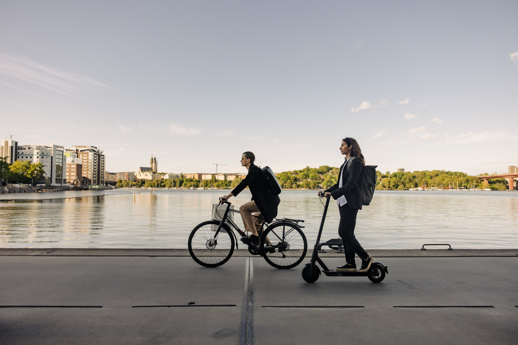 Person on a bicycle and another on an electric scooter by a riverside path