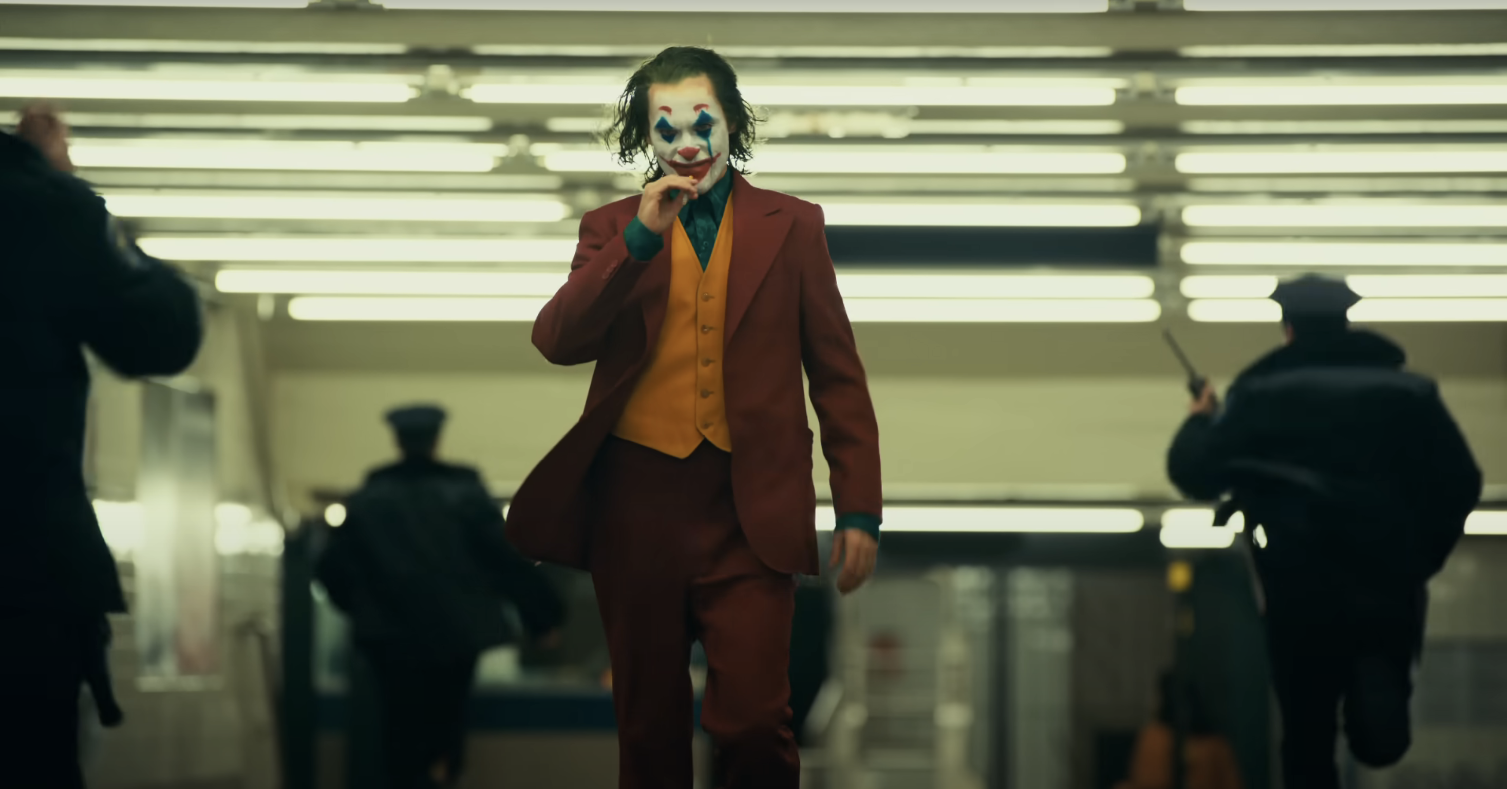 Joaquin Phoenix as Joker in a suit, walking in a train station from the film