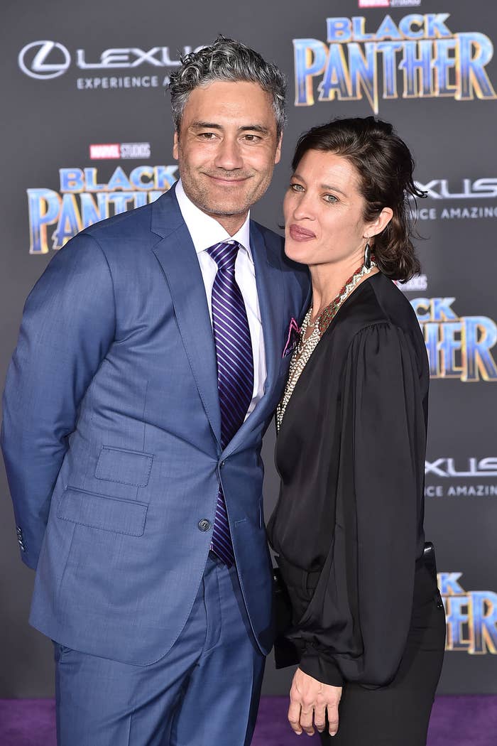 Taika Waititi and Chelsea posing together at the Black Panther event, Waititi in a suit and Chelsea in a blouse