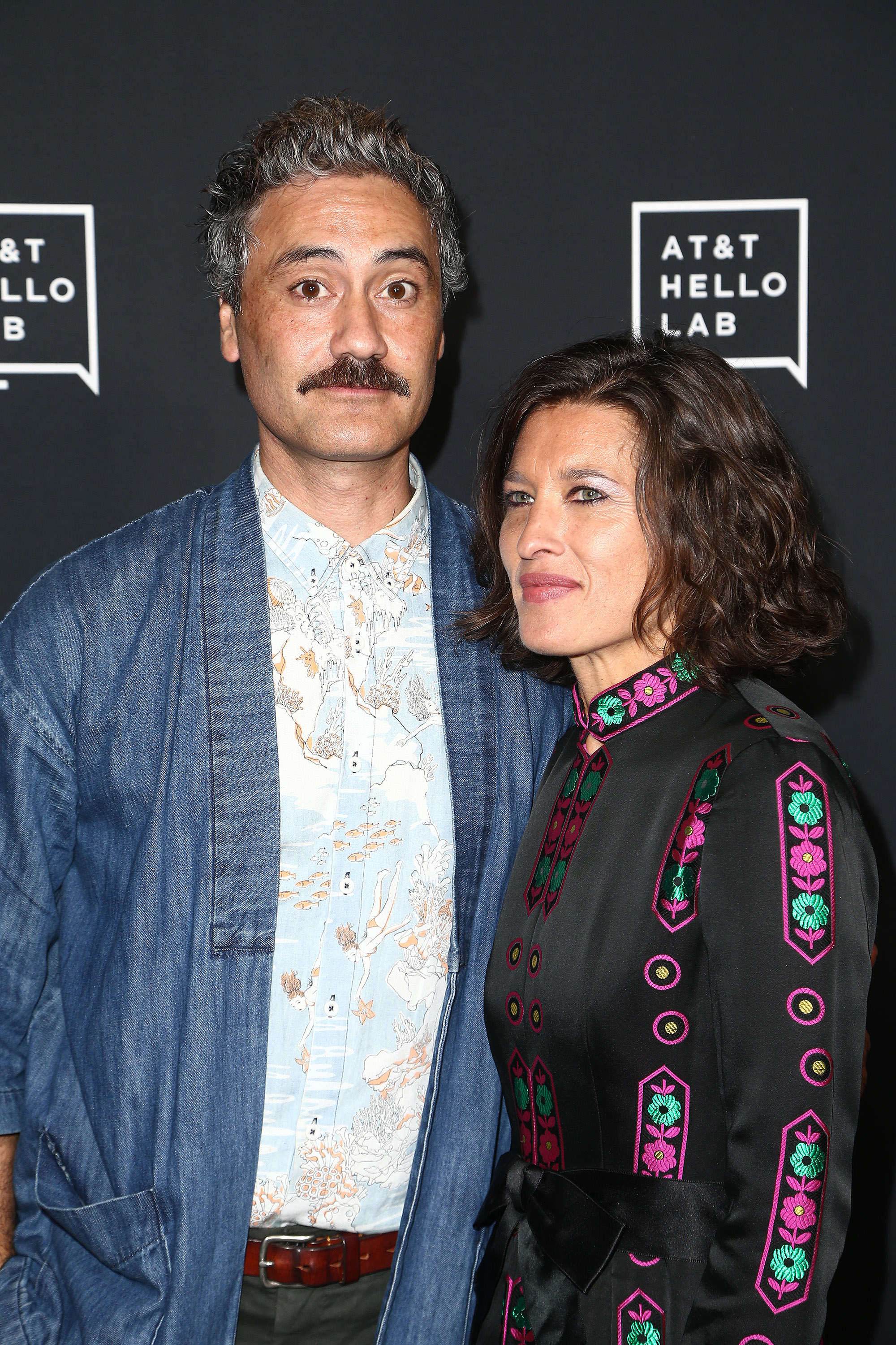 Taika in a denim blazer over a patterned shirt with Chelsea in a black embroidered jacket at a celebrity event