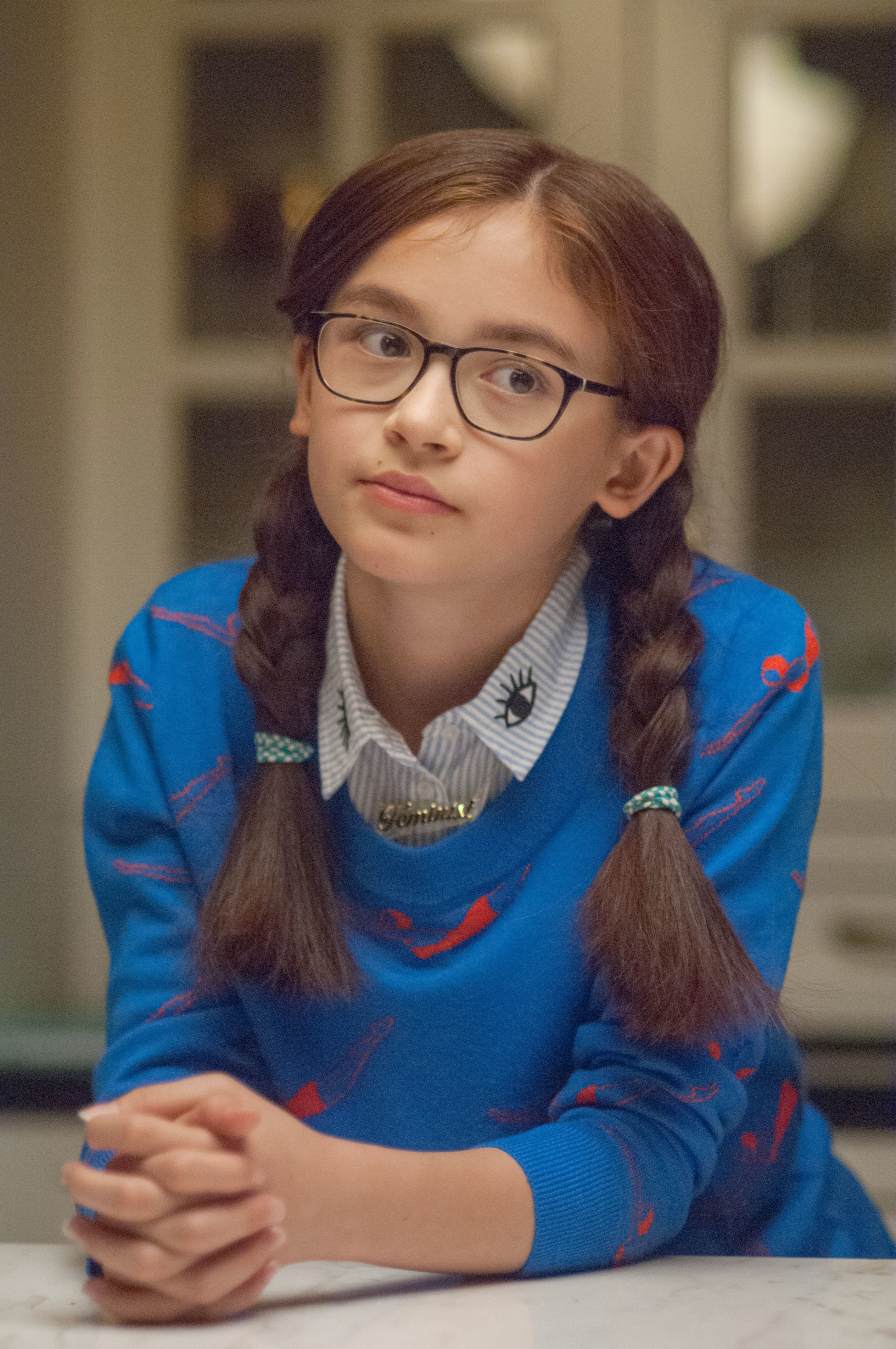 Girl with braided hair and glasses, wearing a sweater, looking thoughtful