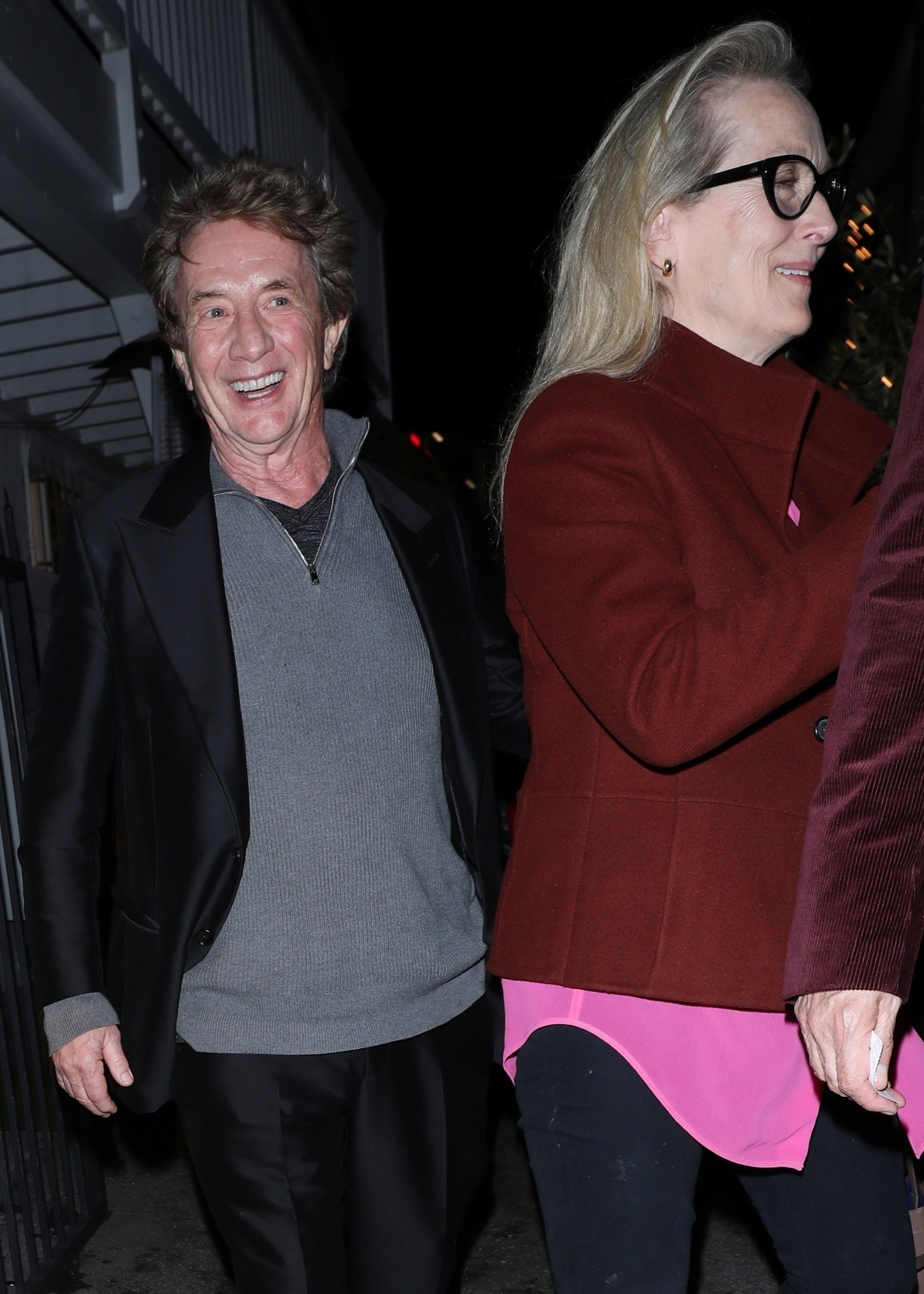 Two individuals walking side by side, one in a black leather jacket, the other in a red cardigan