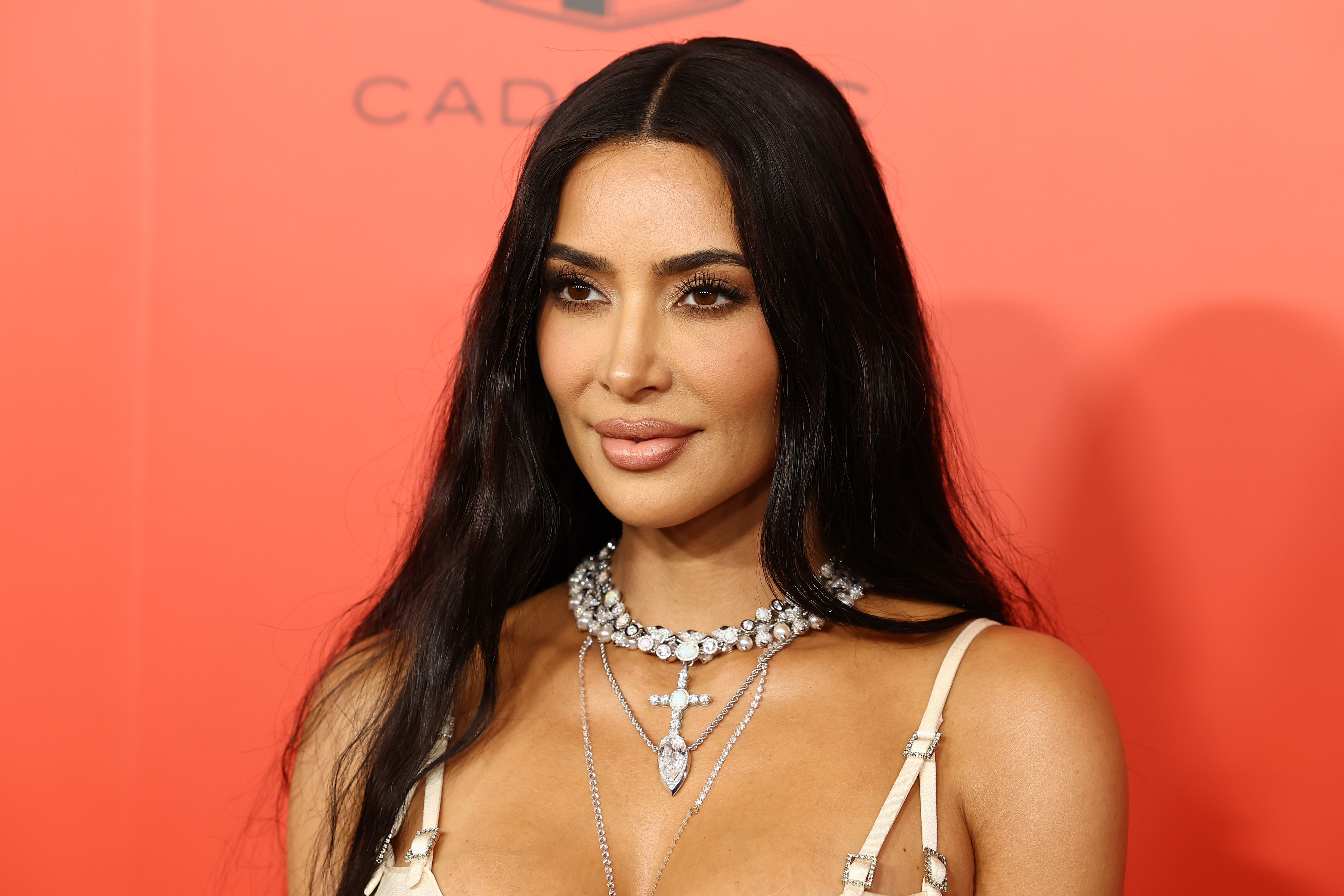 Kim Kardashian posing at an event, wearing a diamond necklace and a strappy dress