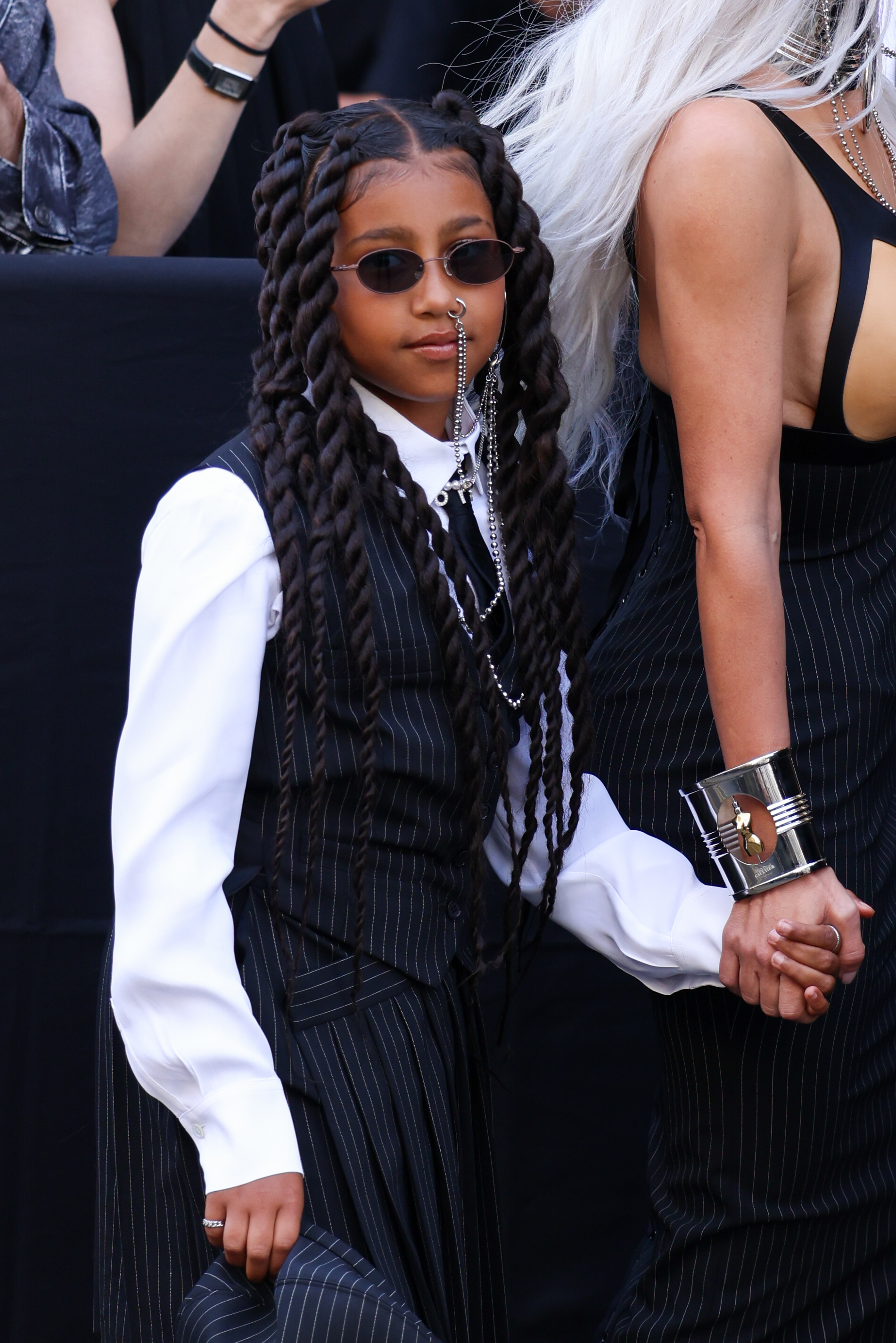 Child in a black striped suit with long braids and sunglasses, holding hands with an adult out of frame
