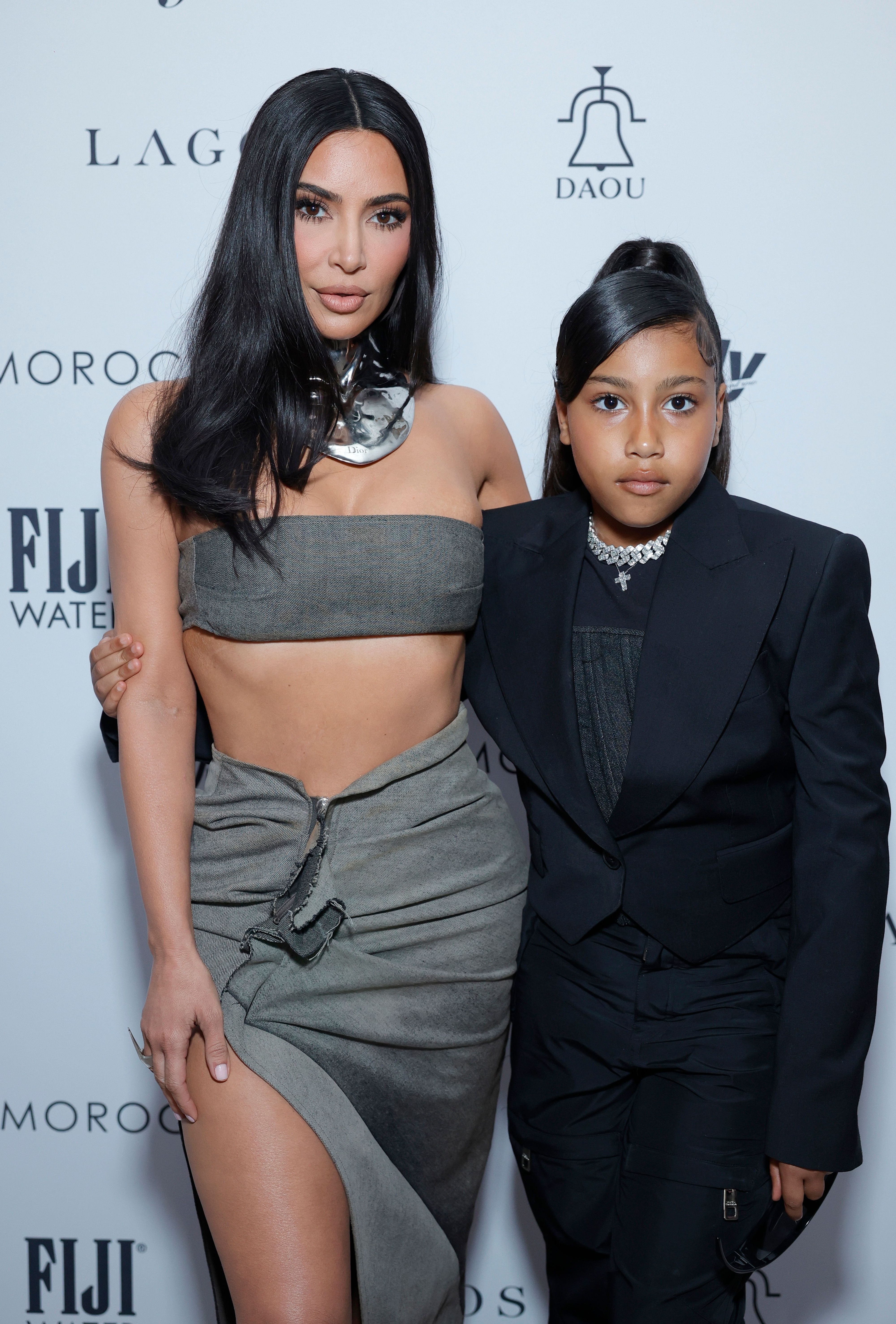 Kim Kardashian in a crop top and skirt with North West in a black suit, both posing at an event