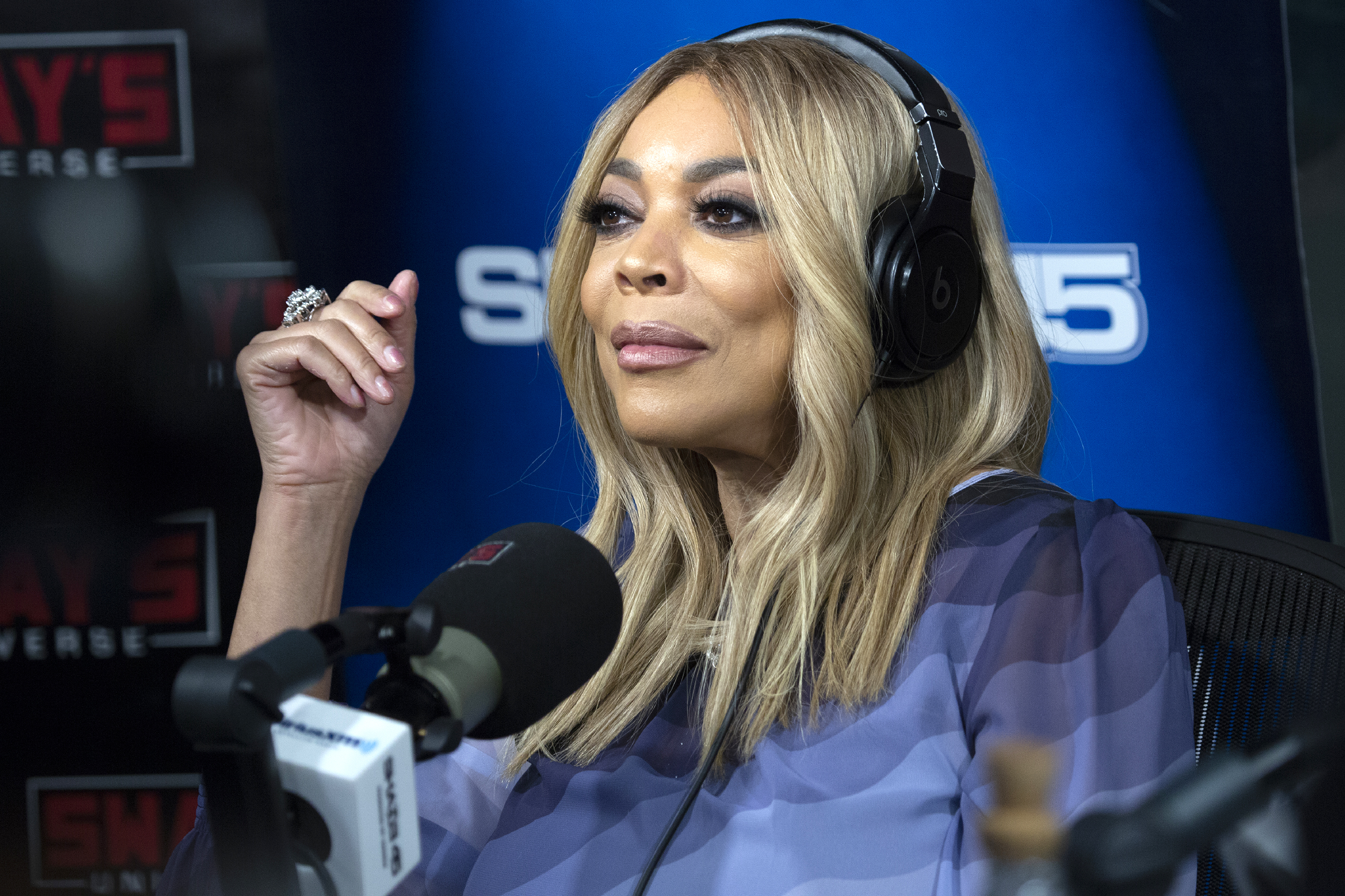 Wendy Williams in a radio studio, wearing headphones, speaking into a mic, styled in a striped garment