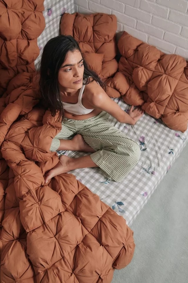 model sitting next to orange diamond puff comforter