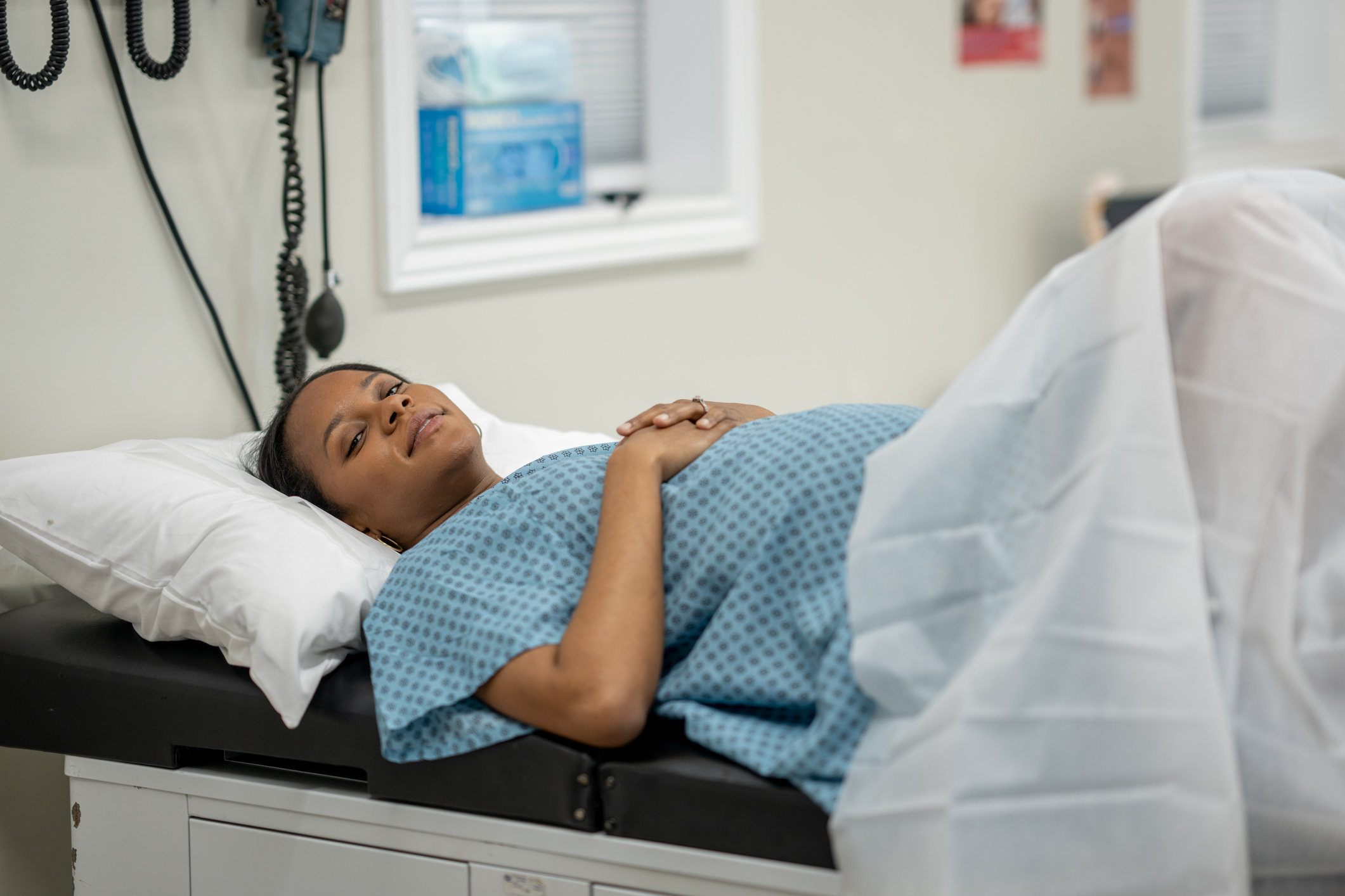 Woman lying in a hospital bed with eyes closed and hands over abdomen
