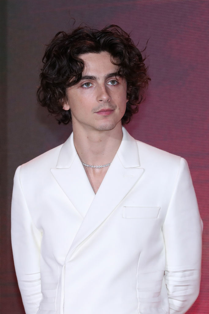 Man in a white buttoned blazer with curly hair at an event
