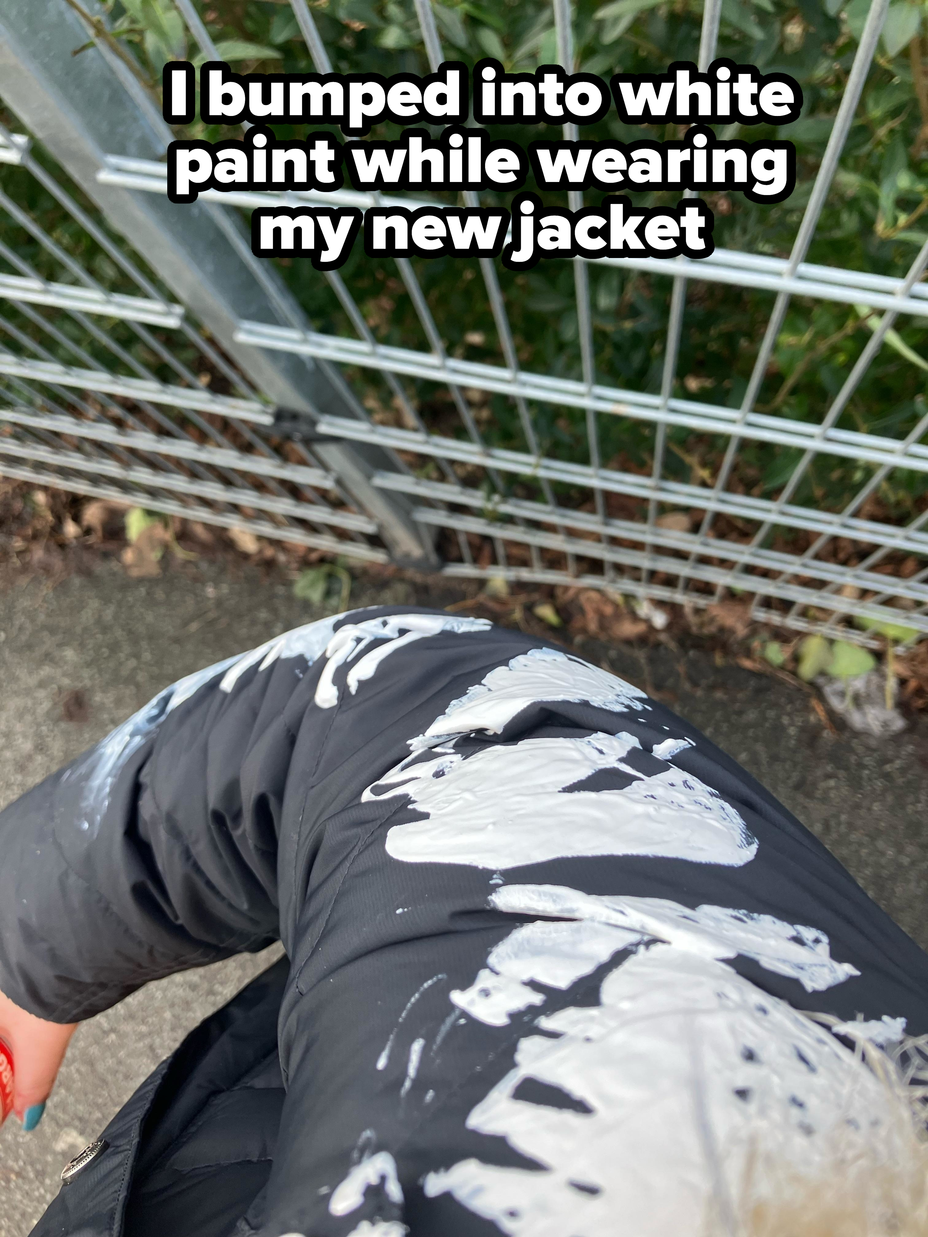 A person&#x27;s new jacket splattered with white paint against a metal fence backdrop