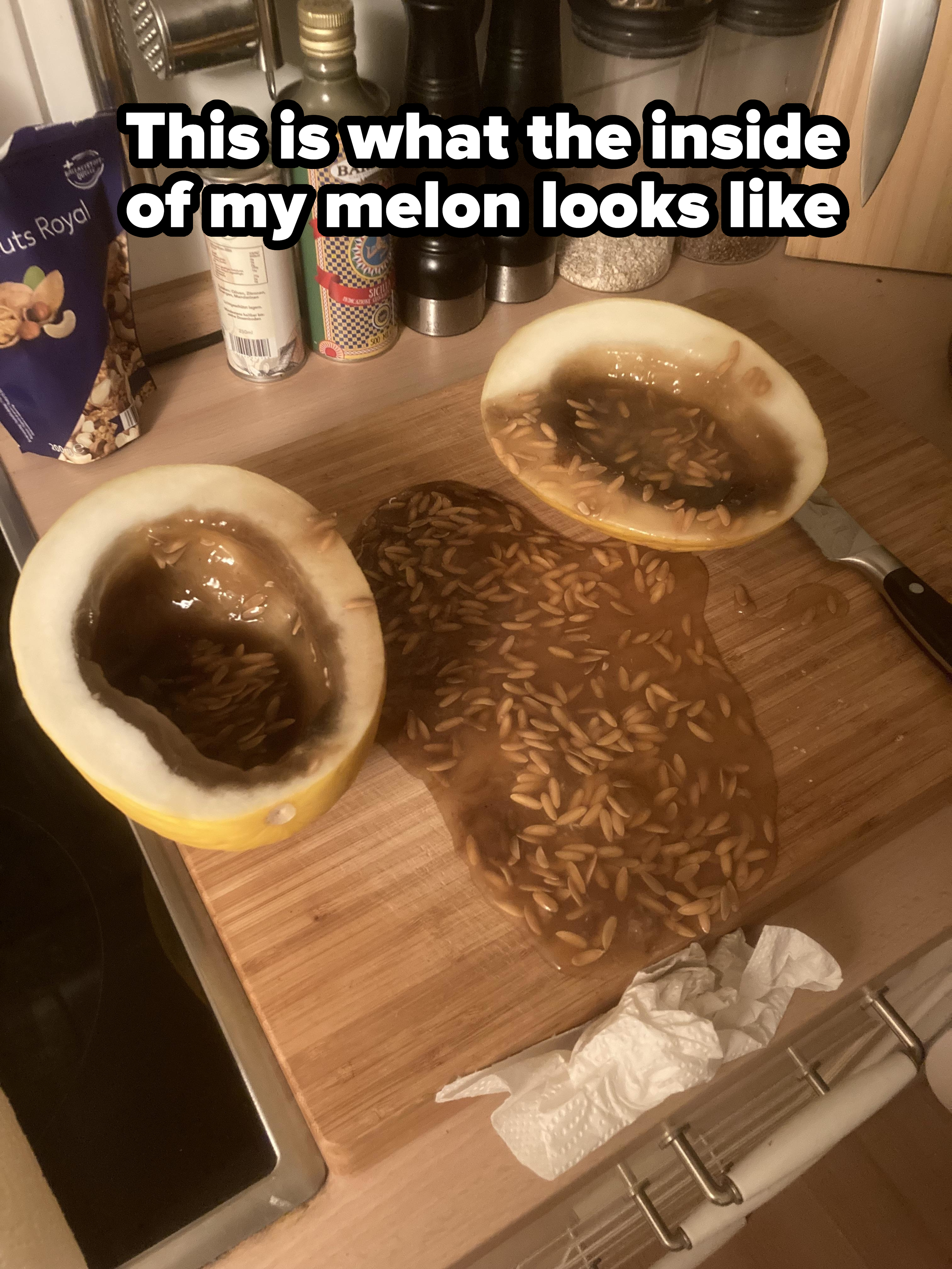 A halved melon with brownish-green liquid and seeds overflowing onto a countertop