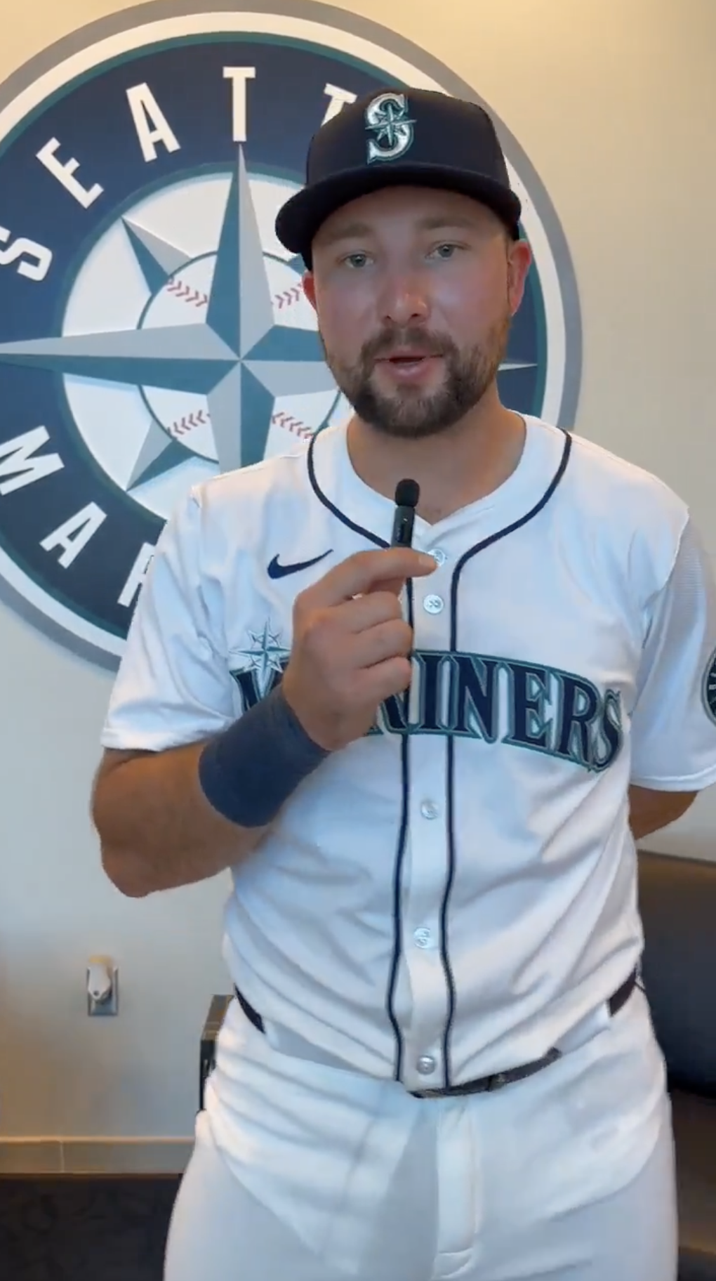 Man in Seattle Mariners baseball uniform speaking into a microphone
