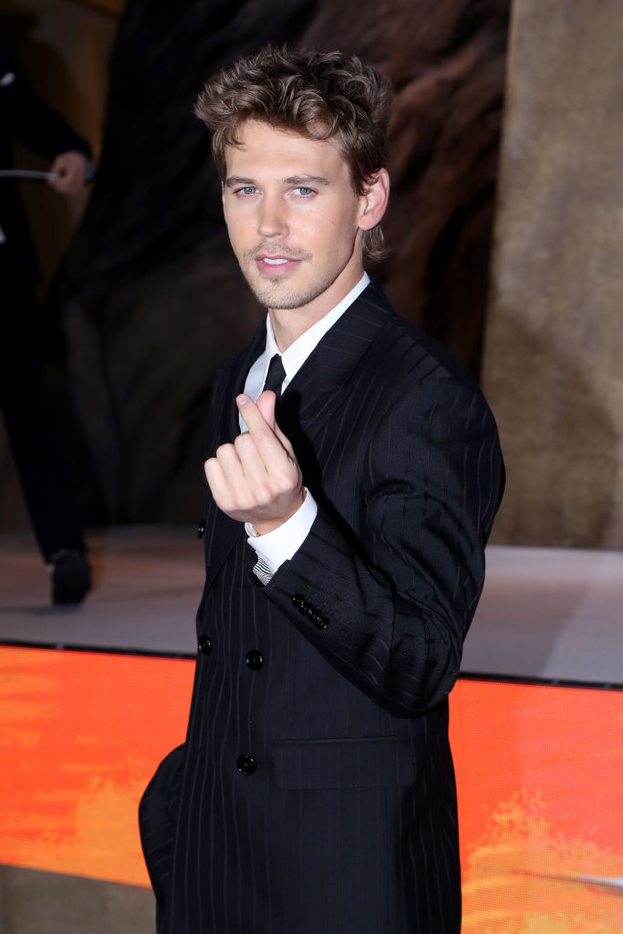 Man in a pinstripe suit poses with a thumbs-up on the red carpet