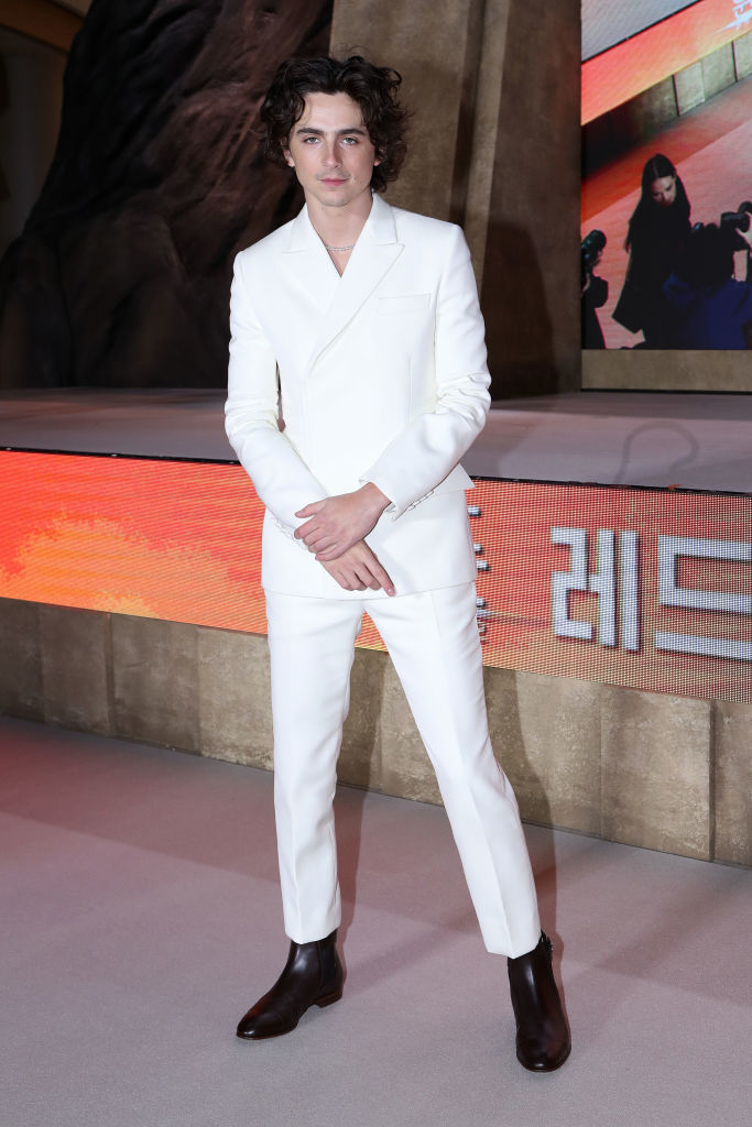 Person in white suit standing before a backdrop with graphic elements