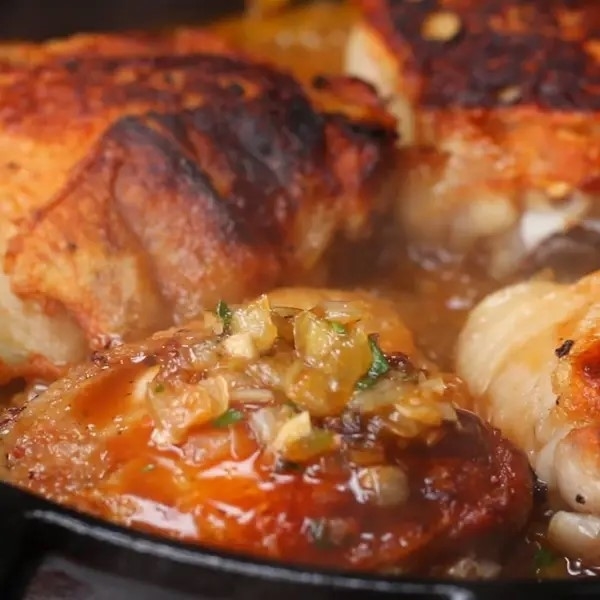 Close-up of a cooked chicken dish in a skillet, with sauce and caramelized onions