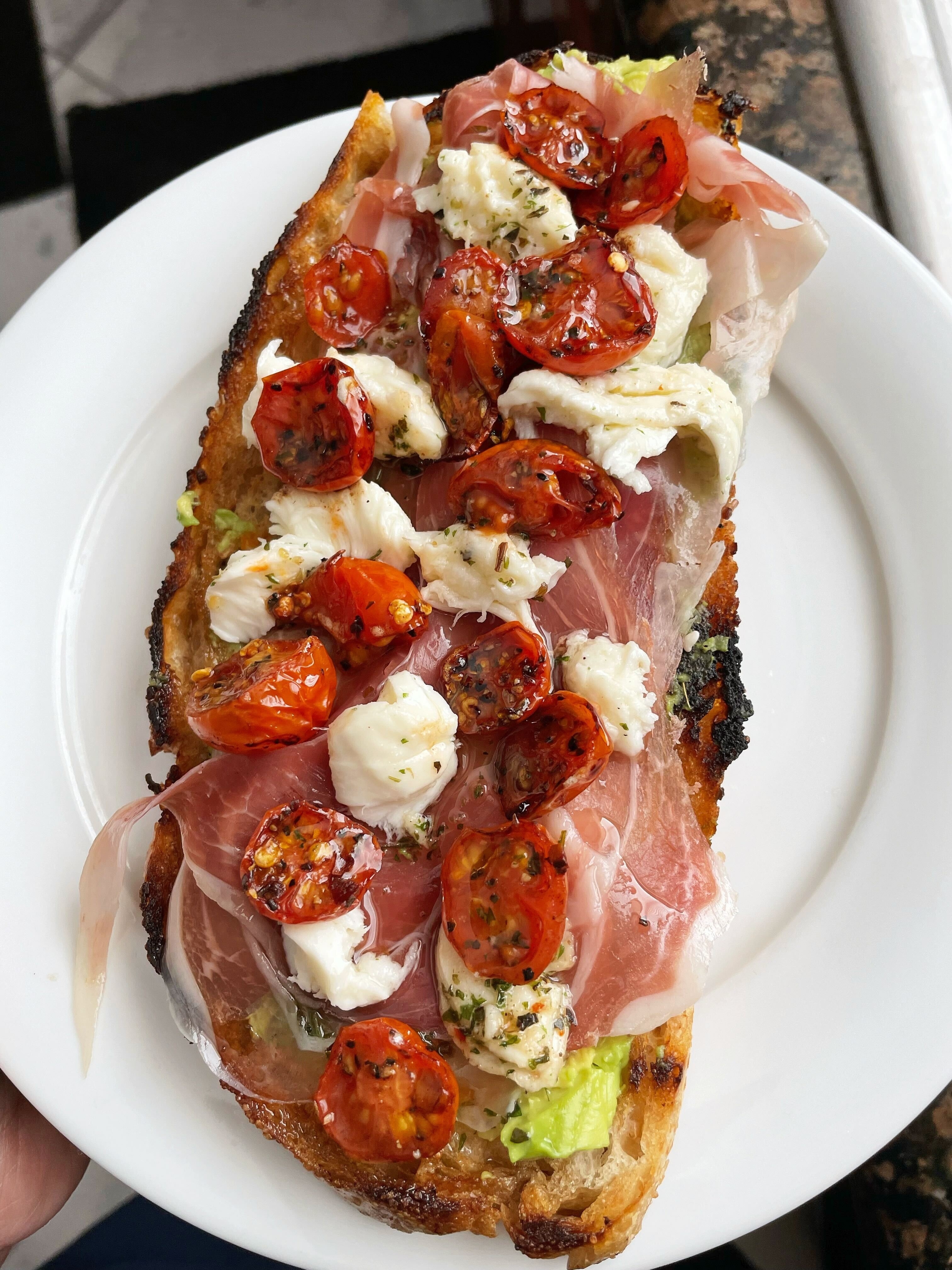 Person holding a plate with bruschetta topped with tomatoes, cheese, and cured meat