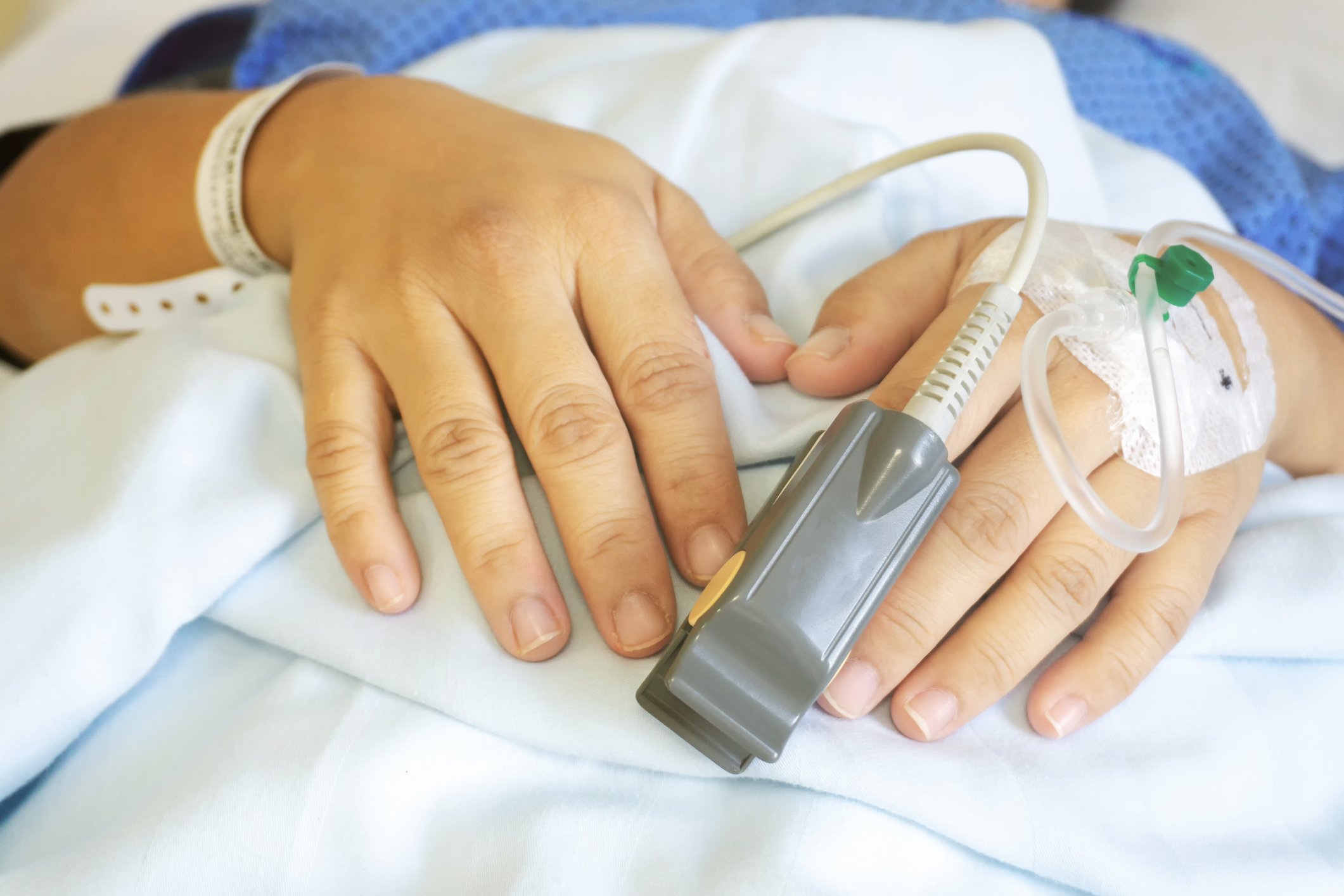 A patient&#x27;s hand with a pulse oximeter attached, resting on a hospital bed
