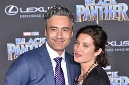 Taika Waititi and Rita Ora posing together at the Black Panther event, Waititi in a suit and Ora in a black blouse