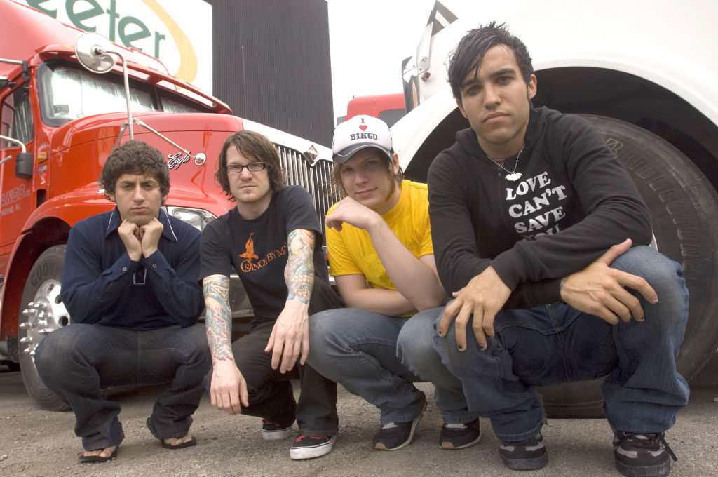 Four members of the band Fall Out Boy posing casually in front of a truck