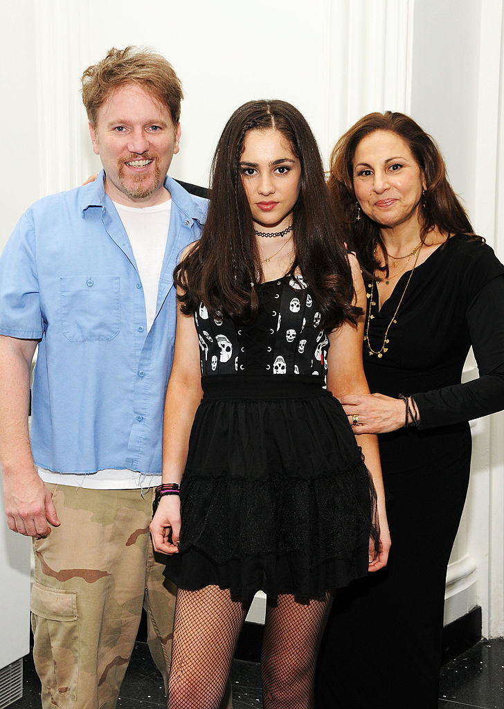 closeup of her standing in the middle of her parents, wearing fishnet tights and a mini dress