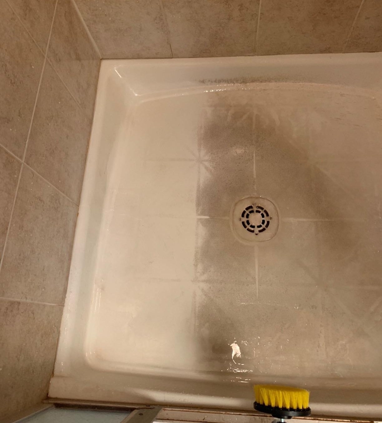 a reviewer photo of a shower stall with dirty marks, part of it cleaned, and a scrub brush on the sid