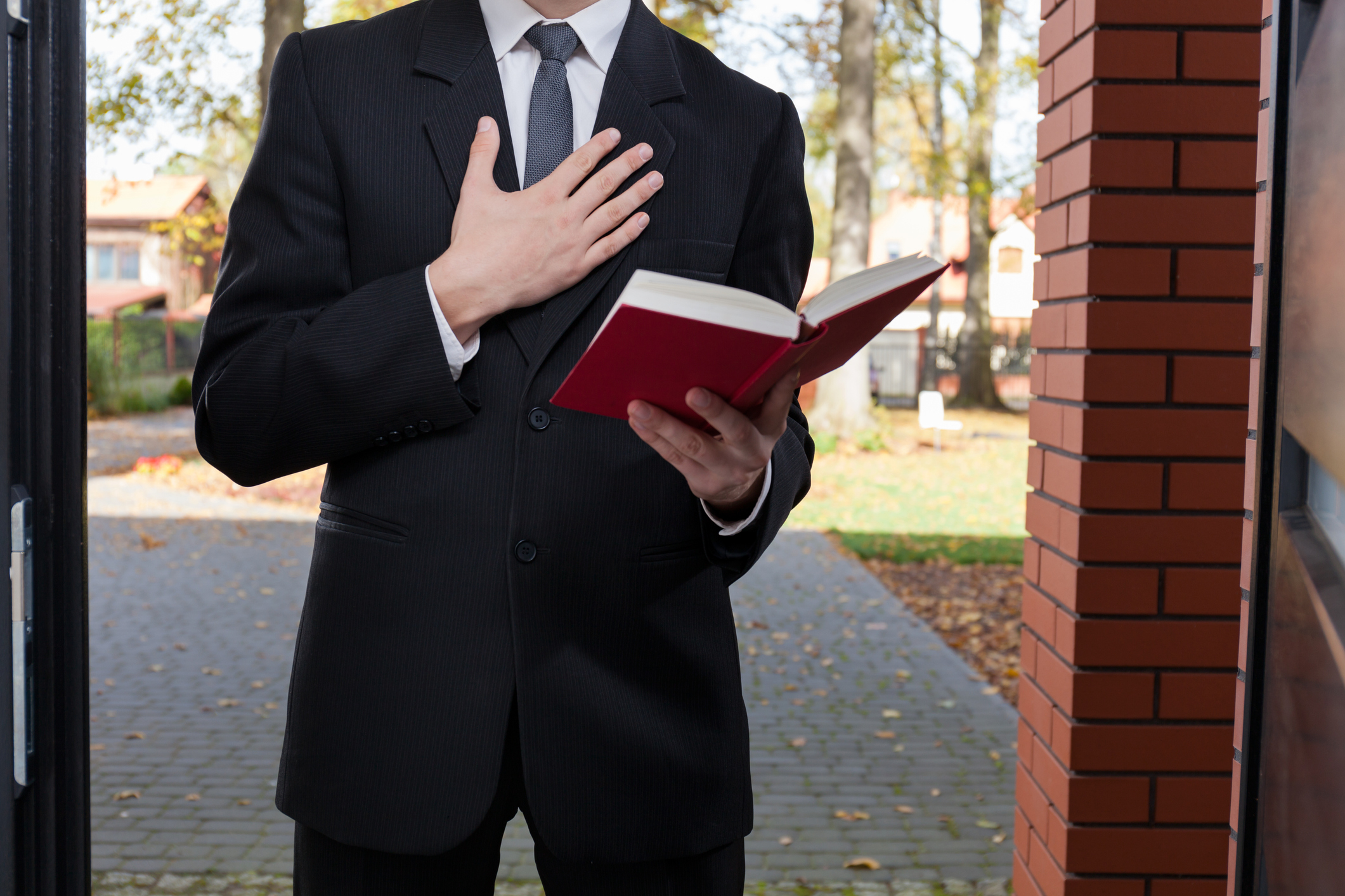 Person in suit reading book with hand on heart standing in doorway