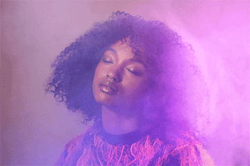 Person with curly hair and eyes closed, surrounded by a hazy, dreamlike effect