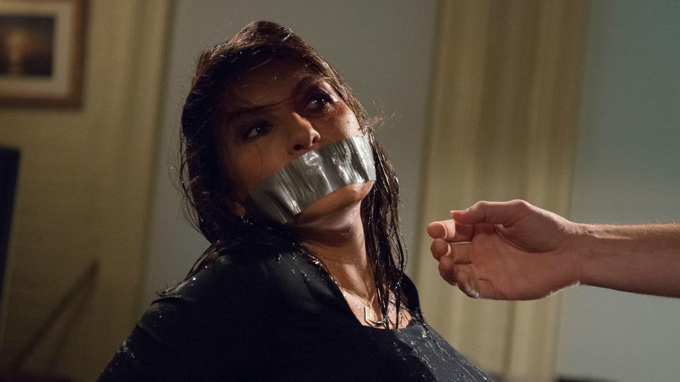 A distressed woman with duct tape over her mouth and wet hair, as a fist is raised near her face