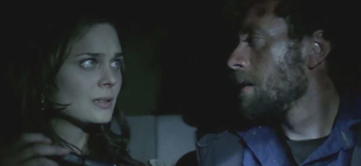 Two characters in a dark setting with concerned expressions; the man is on the right, the woman on the left