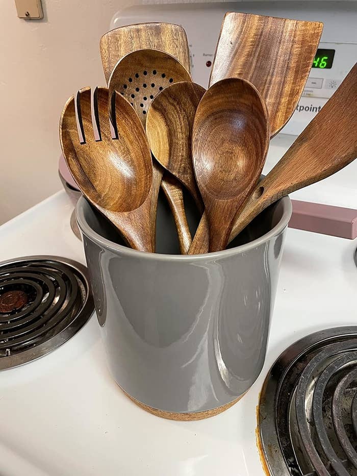 A variety of wooden cooking utensils in a gray holder on a stovetop. Perfect for home chefs looking for natural kitchen tools