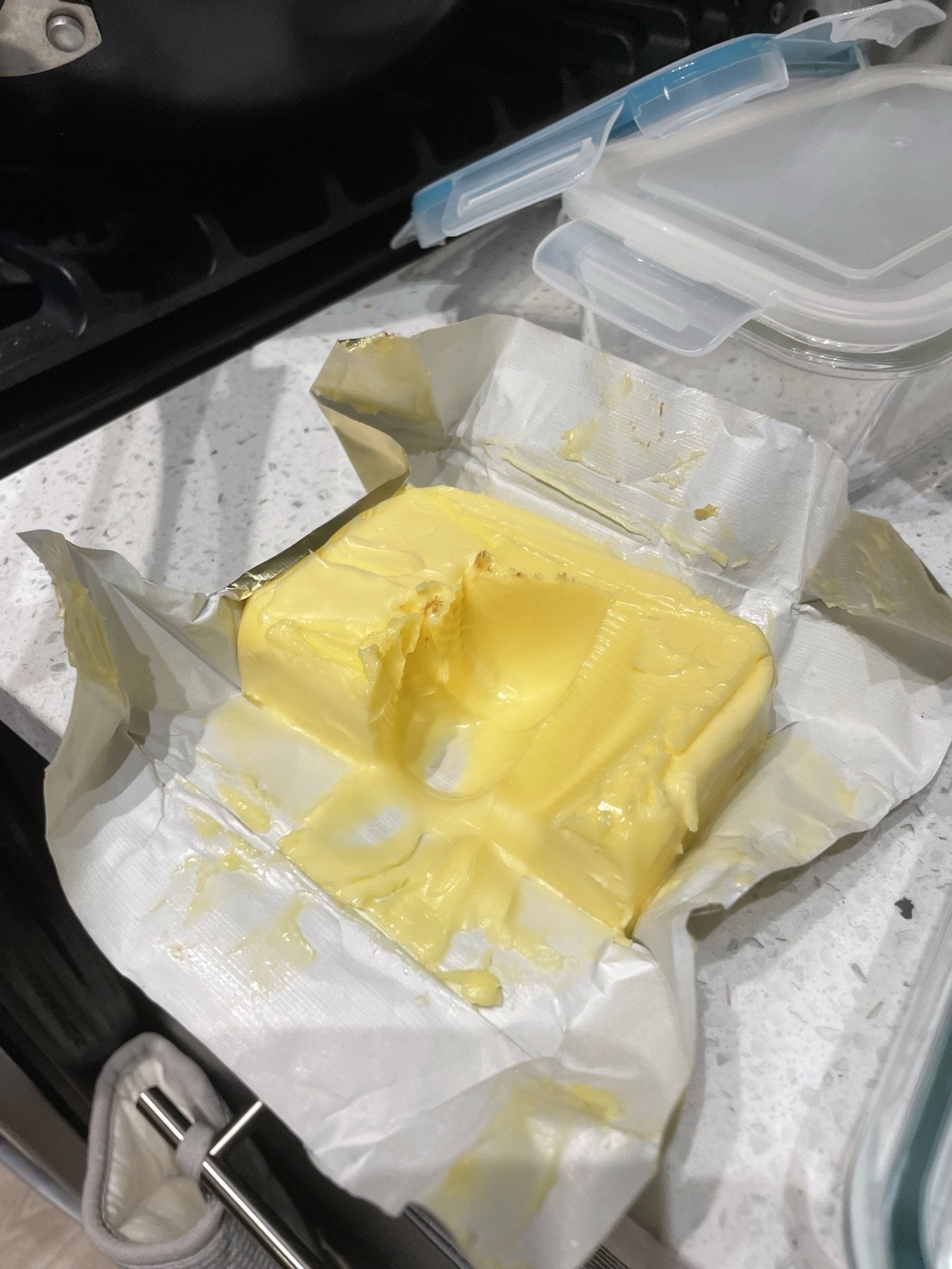 Partial stick of butter with scoop taken out, on open wrapper near containers